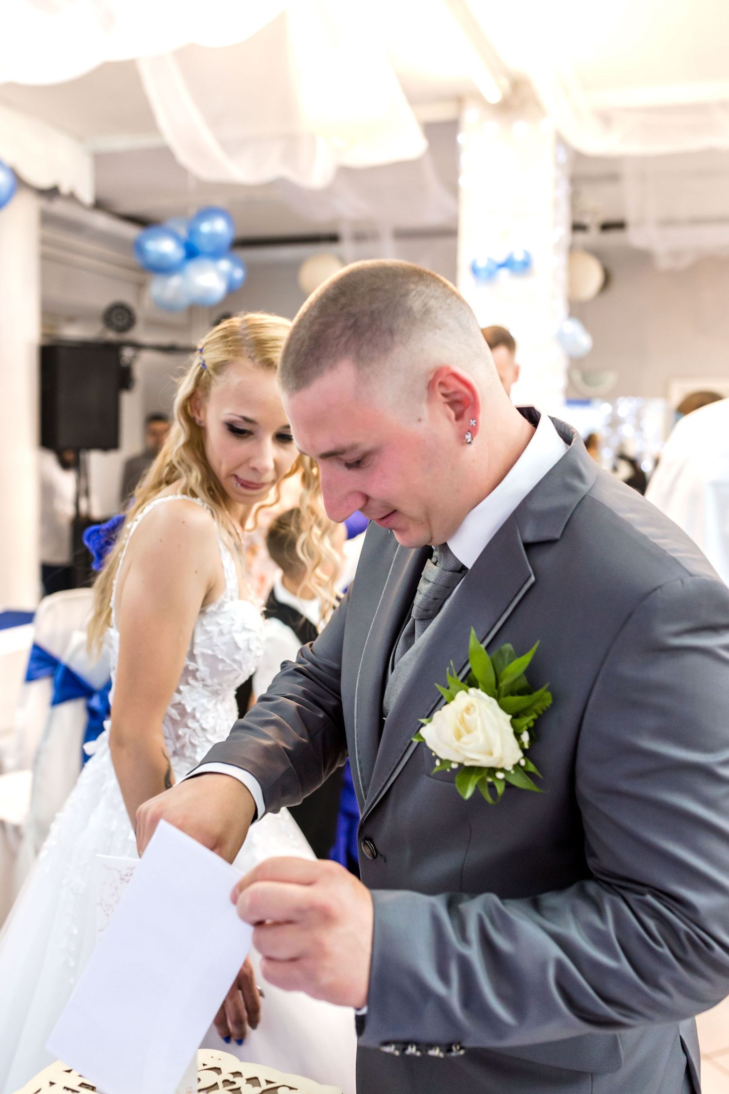 Emotional moment at a wedding reception with people in gray suits and white decor with blue accents.
