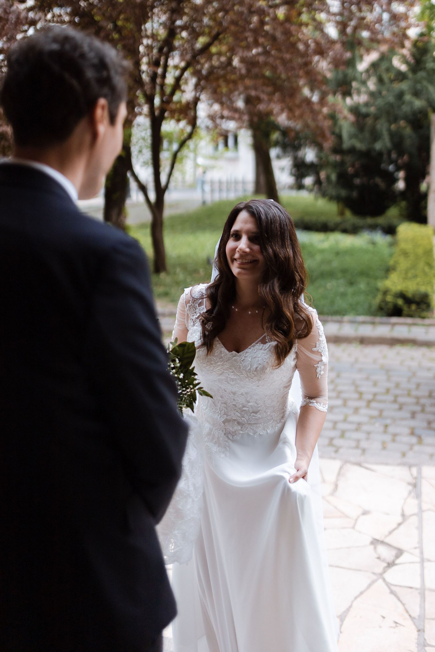 A couple shares a romantic moment in a garden setting during their wedding ceremony, with autumn trees in the background.