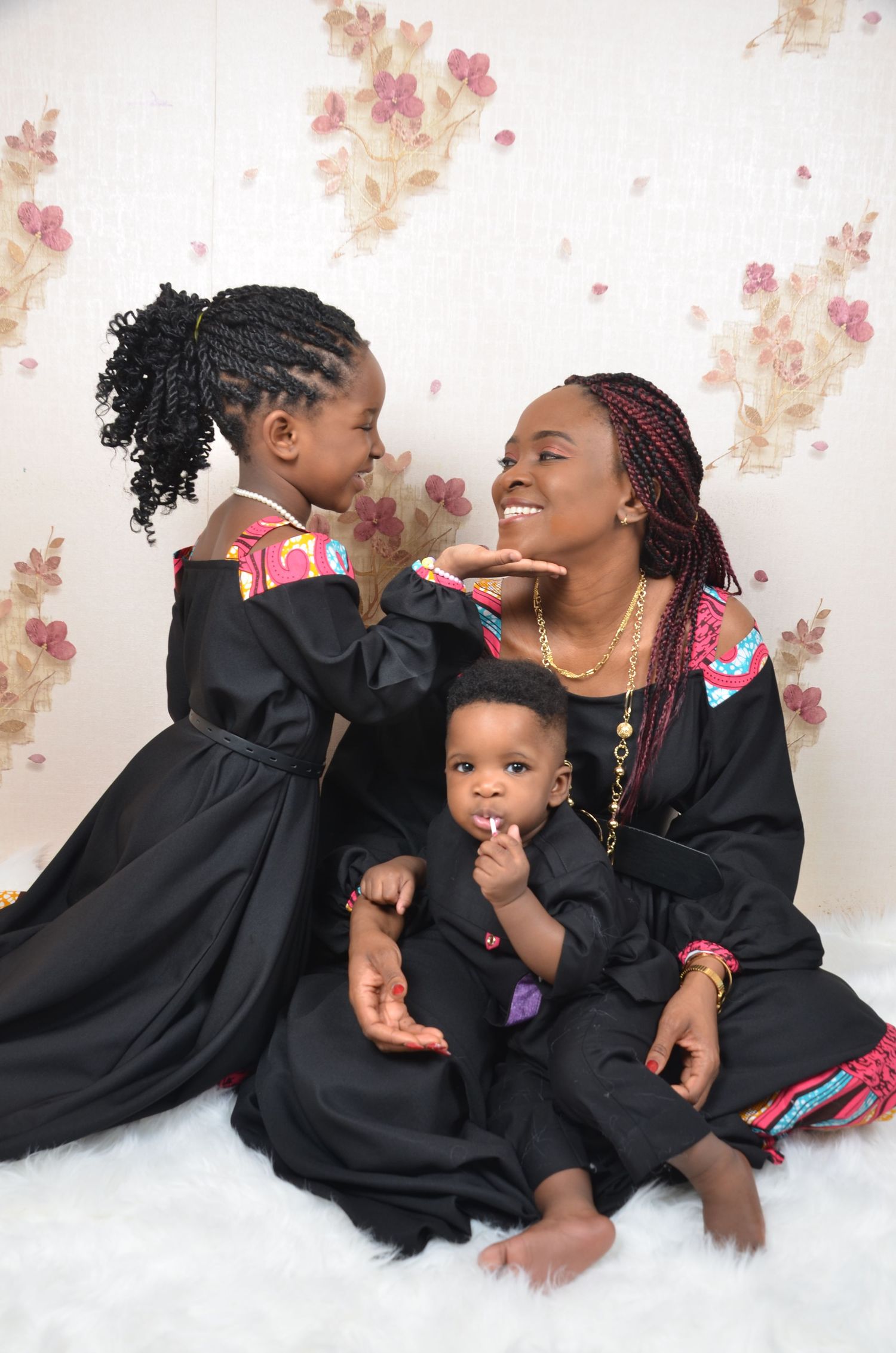 Family portrait featuring matching black outfits against floral backdrop.