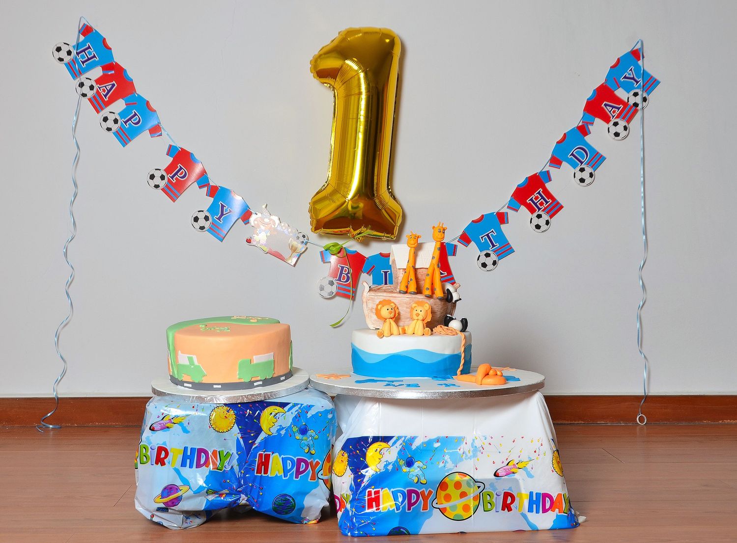 First birthday party setup with two cakes, gold number 1 balloon, and soccer-themed banner decorations.