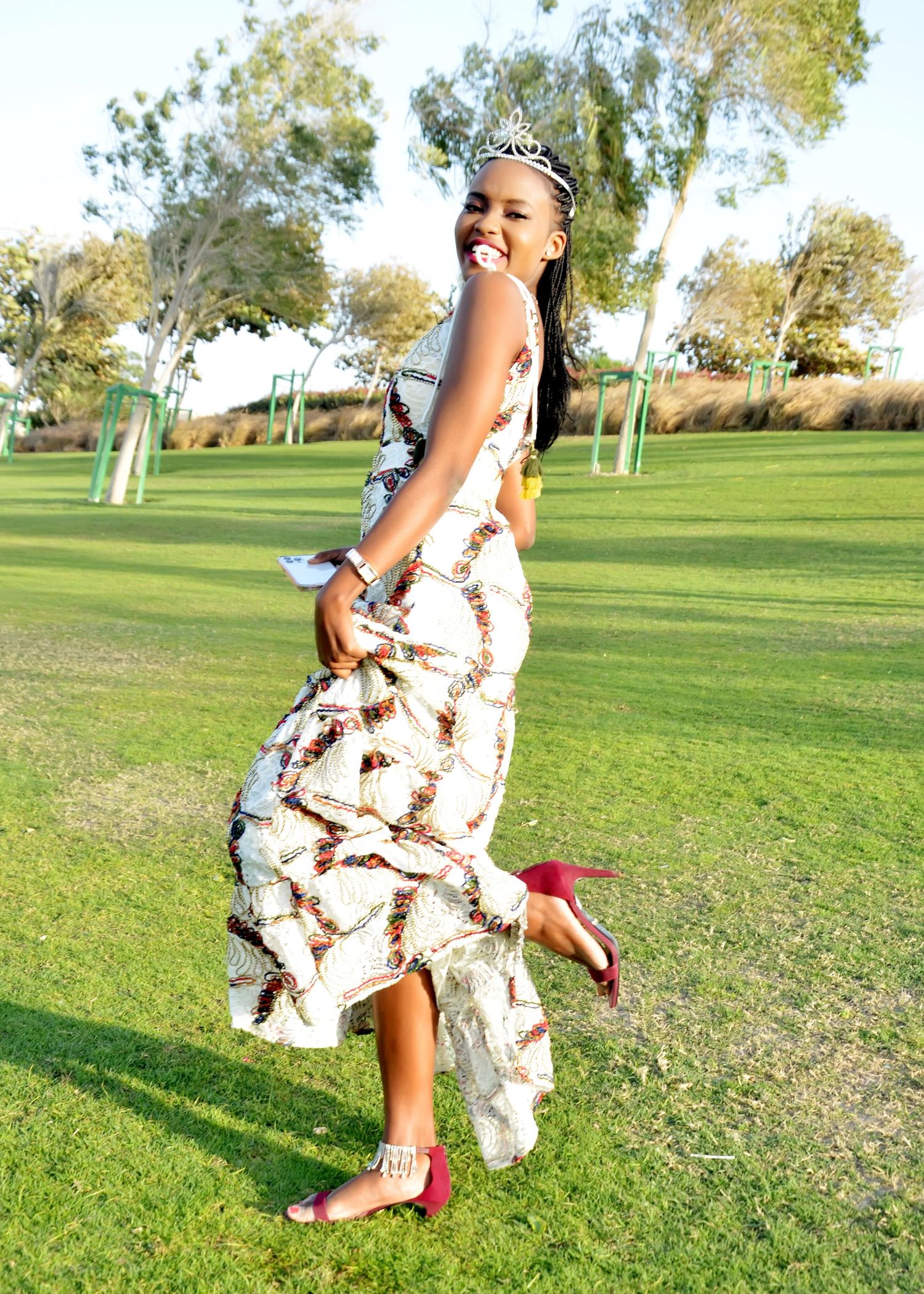 A playful twirl in a patterned white dress and red shoes on grassy grounds.