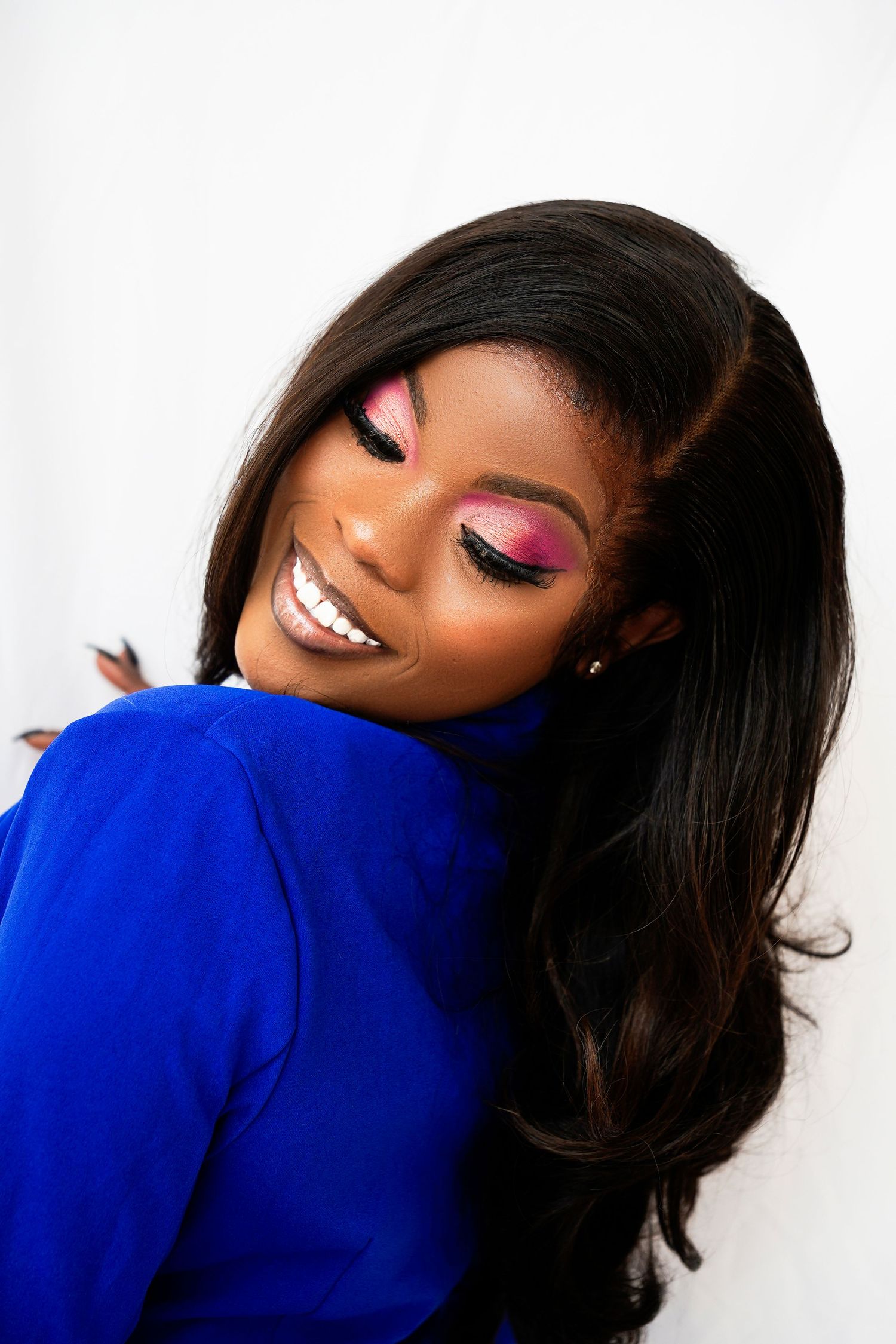 Portrait of woman in bright blue sweater with colorful eye makeup and glossy hair.