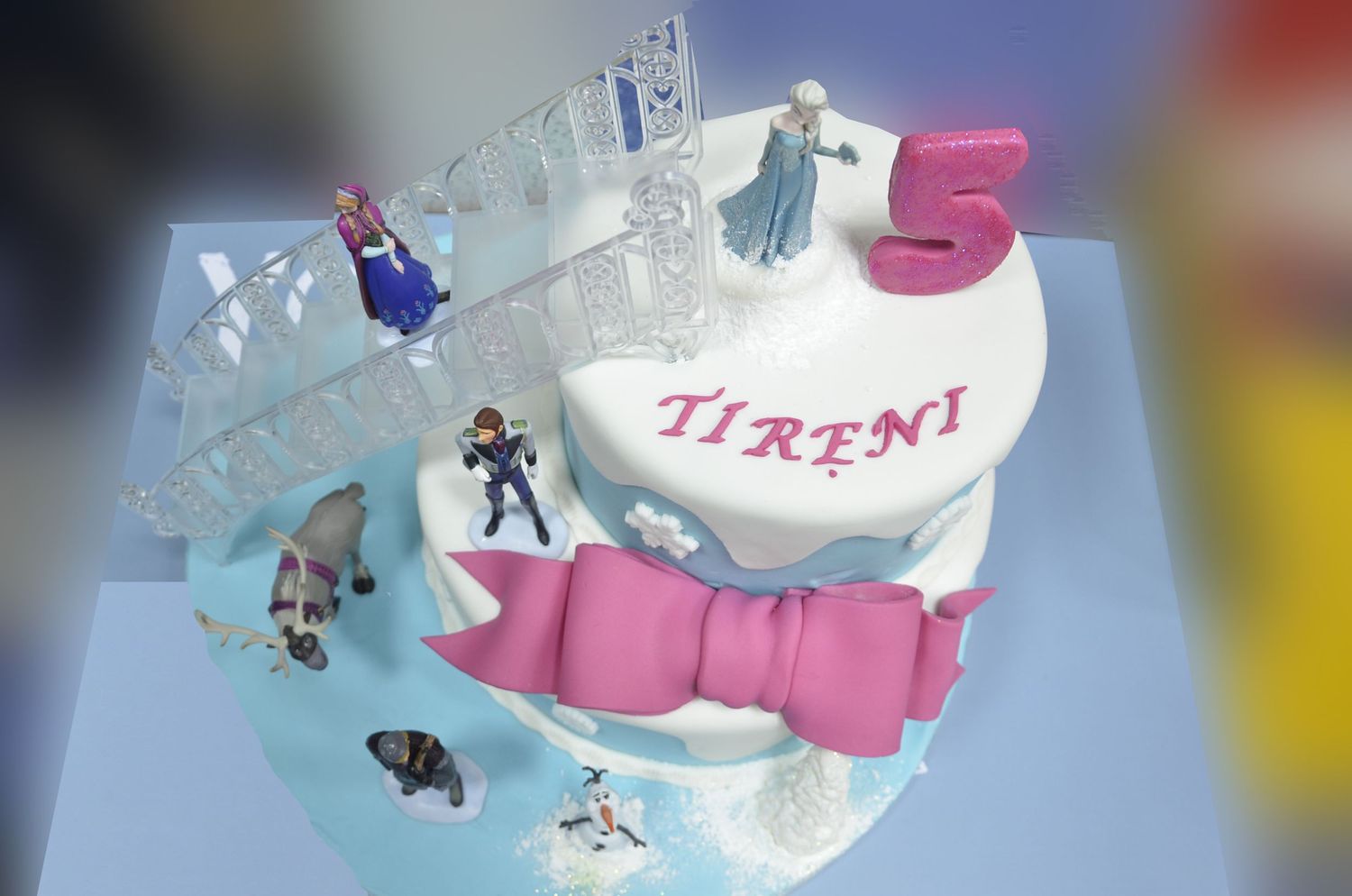 A Frozen-themed birthday cake with ice crystal decorations and a pink bow on a blue background.