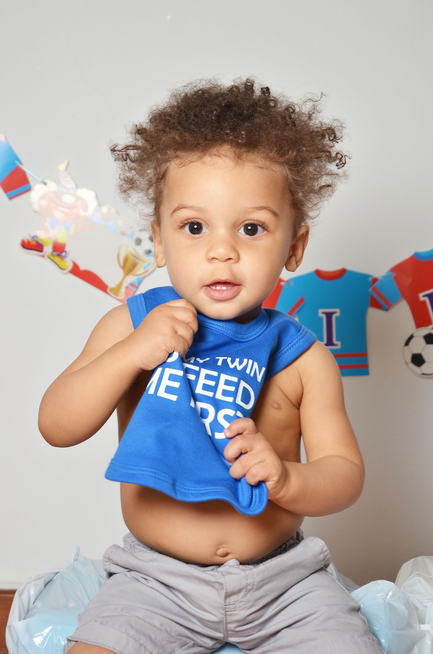 Baby in blue bib sitting on floor with festive decorations and streamers in red and blue colors.