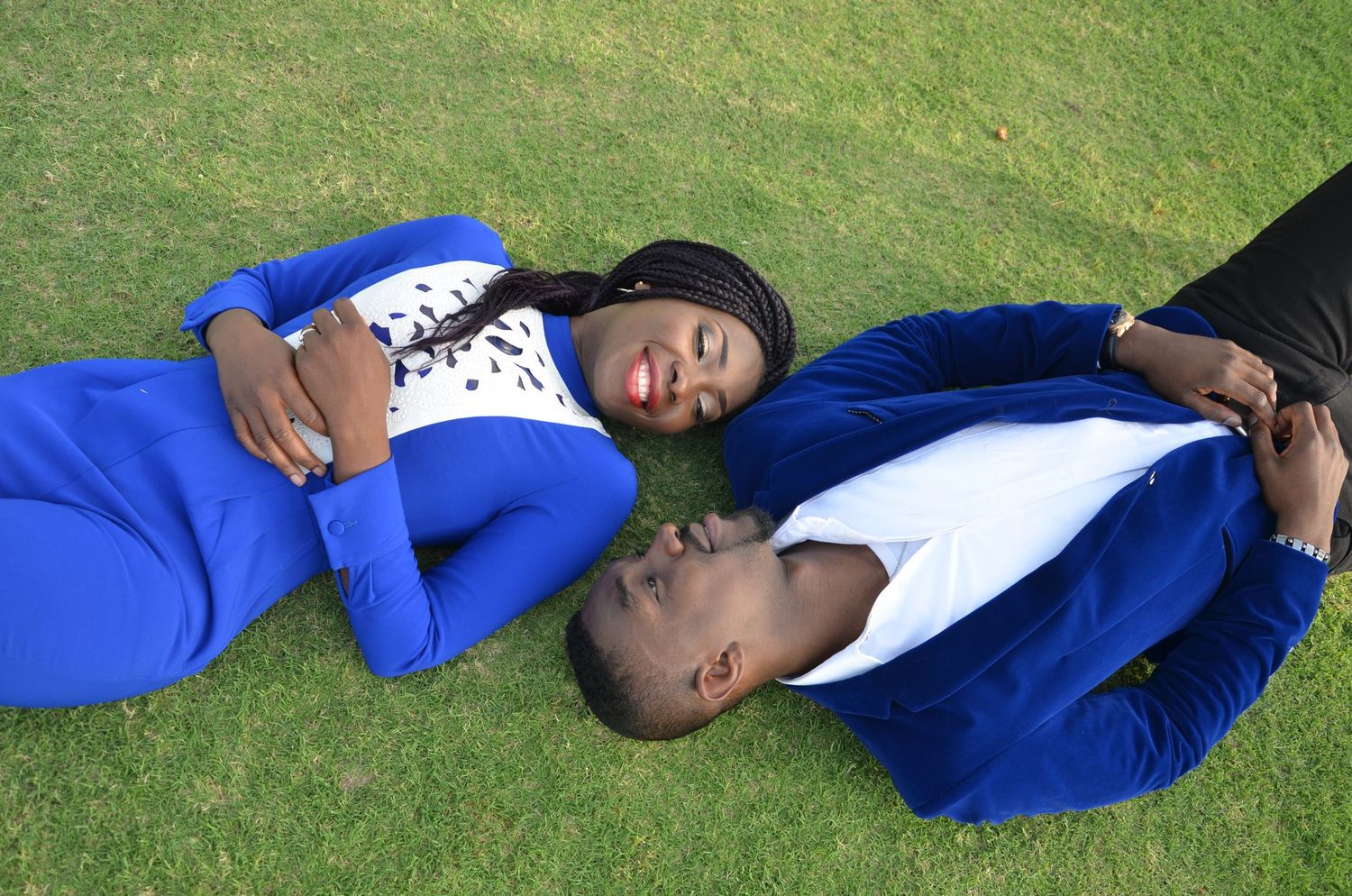 Person in blue jacket lying on green grass in casual pose.