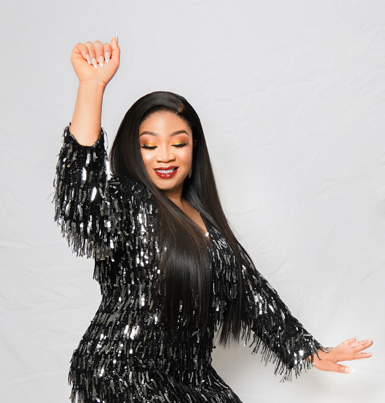 A model in a black sequined fringe dress dances joyfully against a grey background.