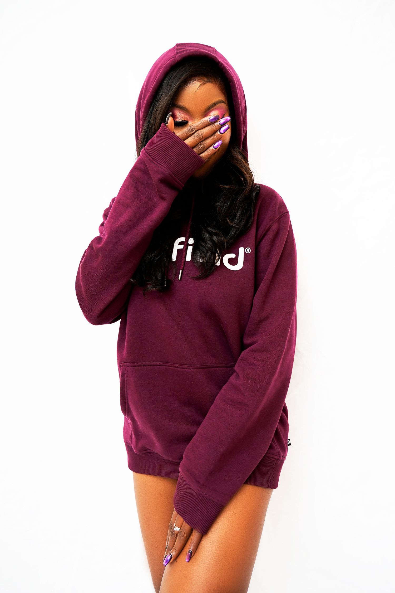 Fashion model in burgundy Fila hoodie with decorated nails covering face.