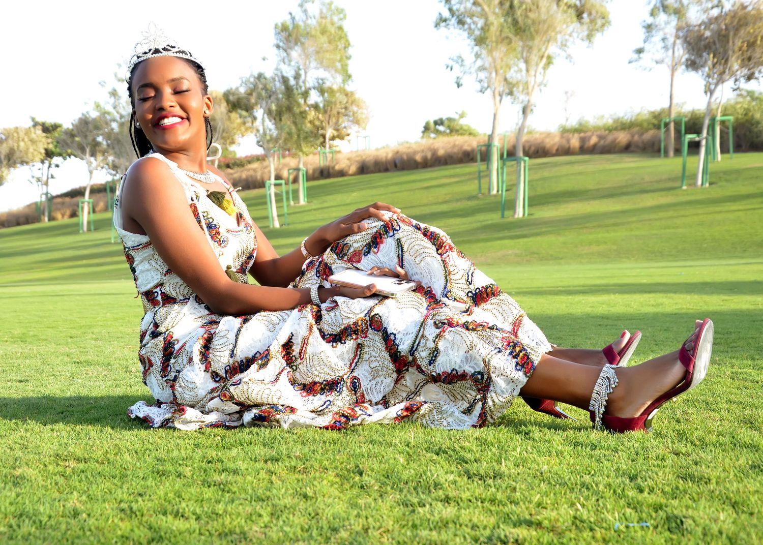 A flowy white patterned maxi dress is styled with heels against a lush green golf course backdrop.