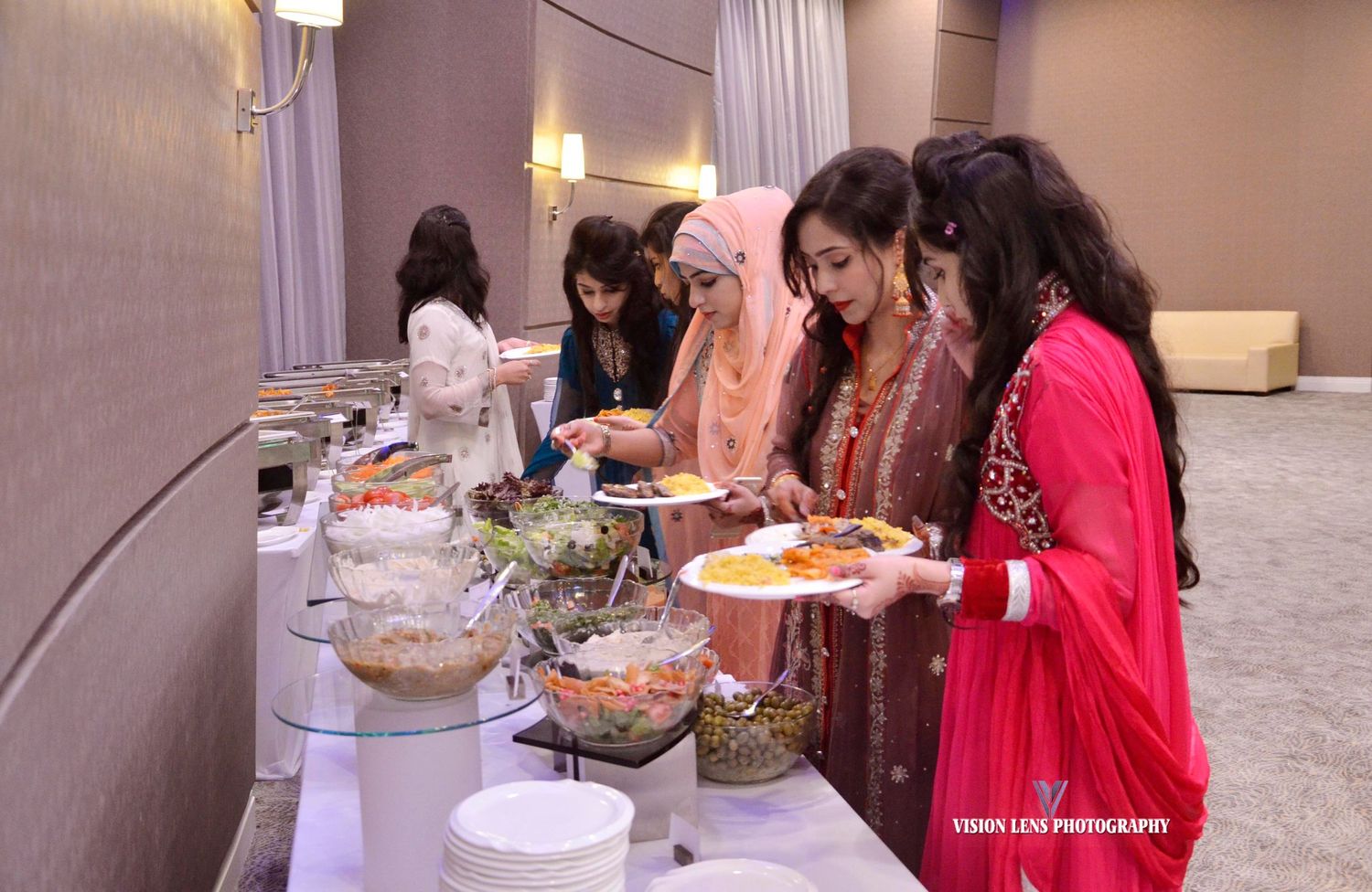 Group of people serving themselves food from a buffet line at an elegant event.