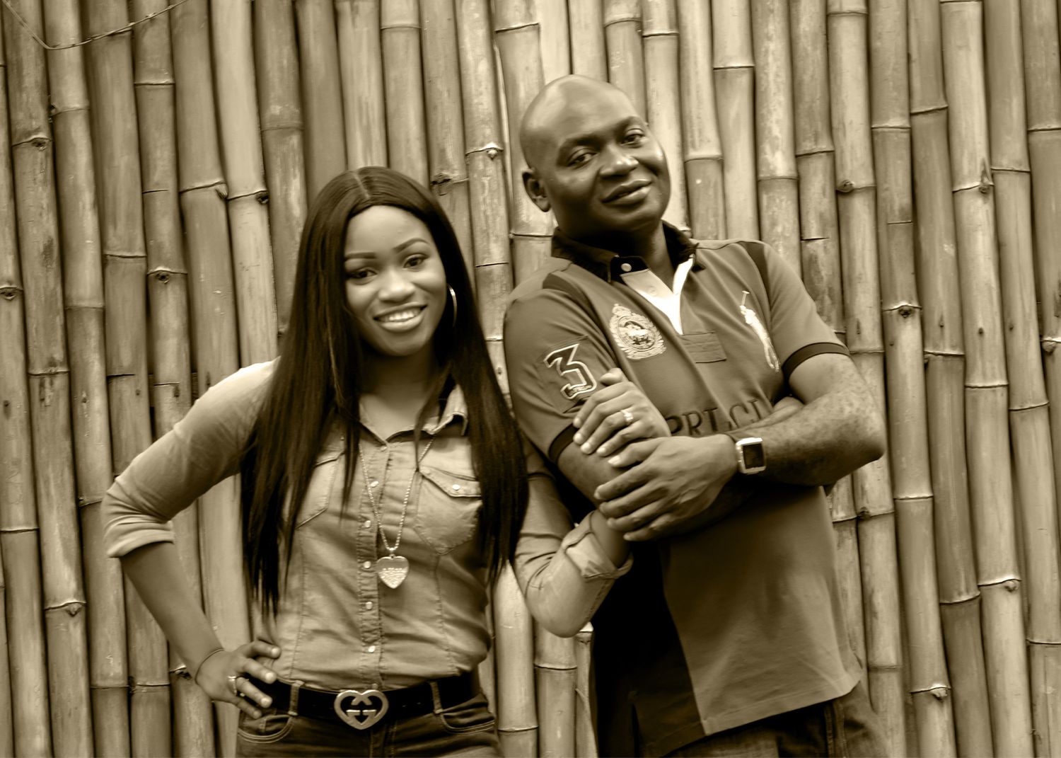 A sepia-toned portrait of two people posing against a bamboo wall backdrop.