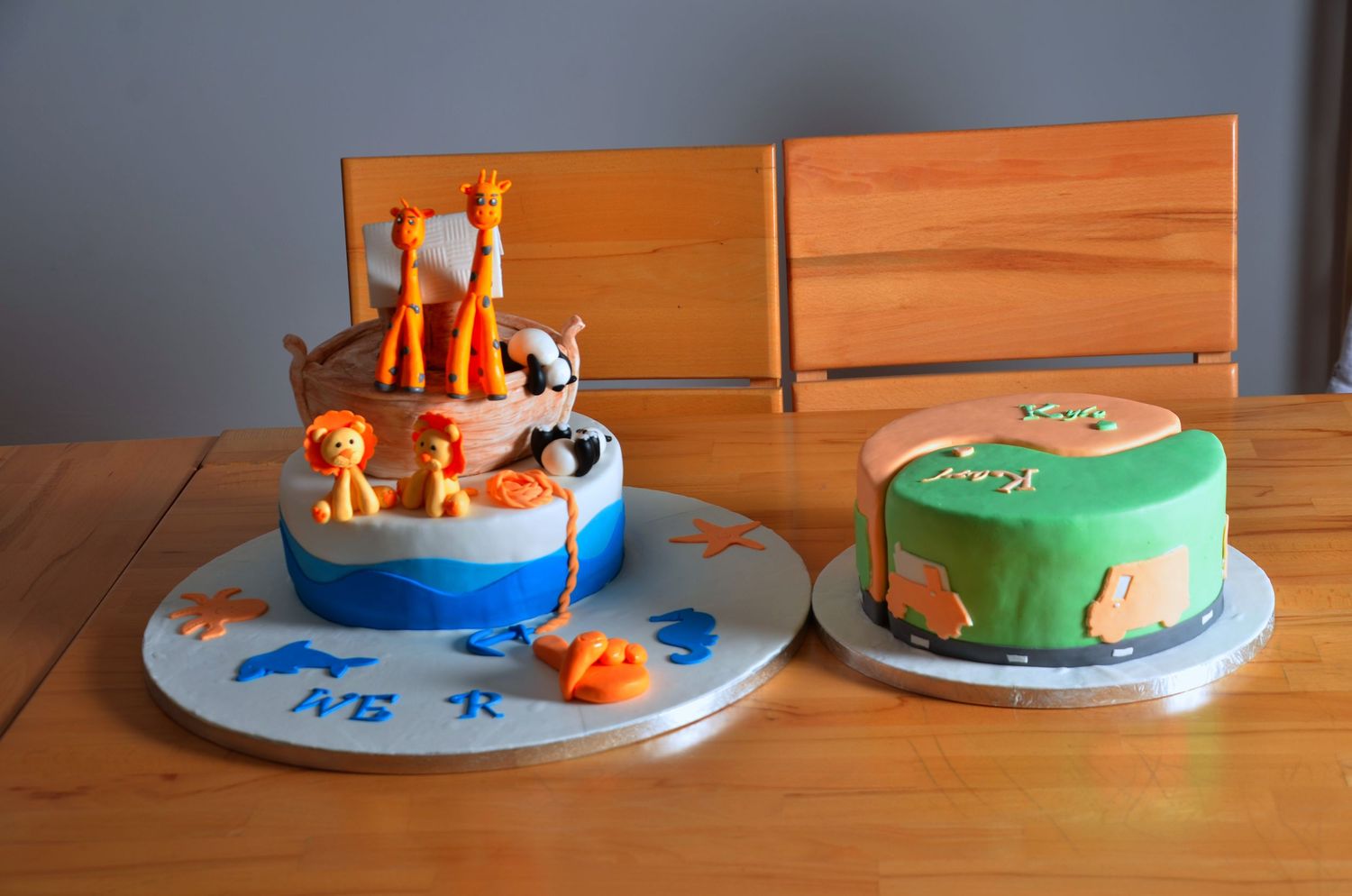 Two themed birthday cakes on a wooden table, one with animals and another with green frosting.