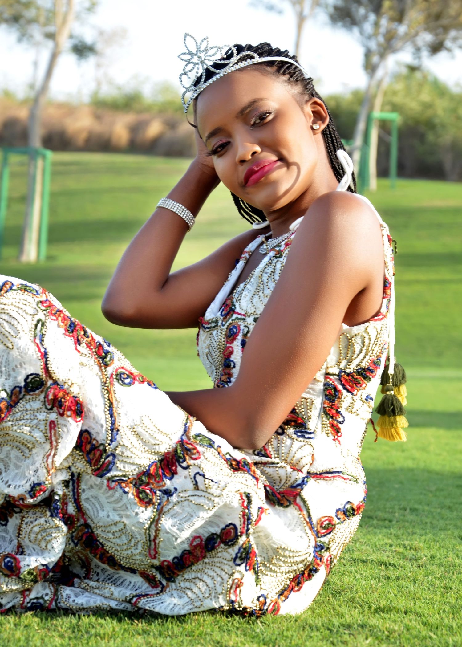 A model relaxes on grass wearing a patterned summer dress and decorative headpiece.