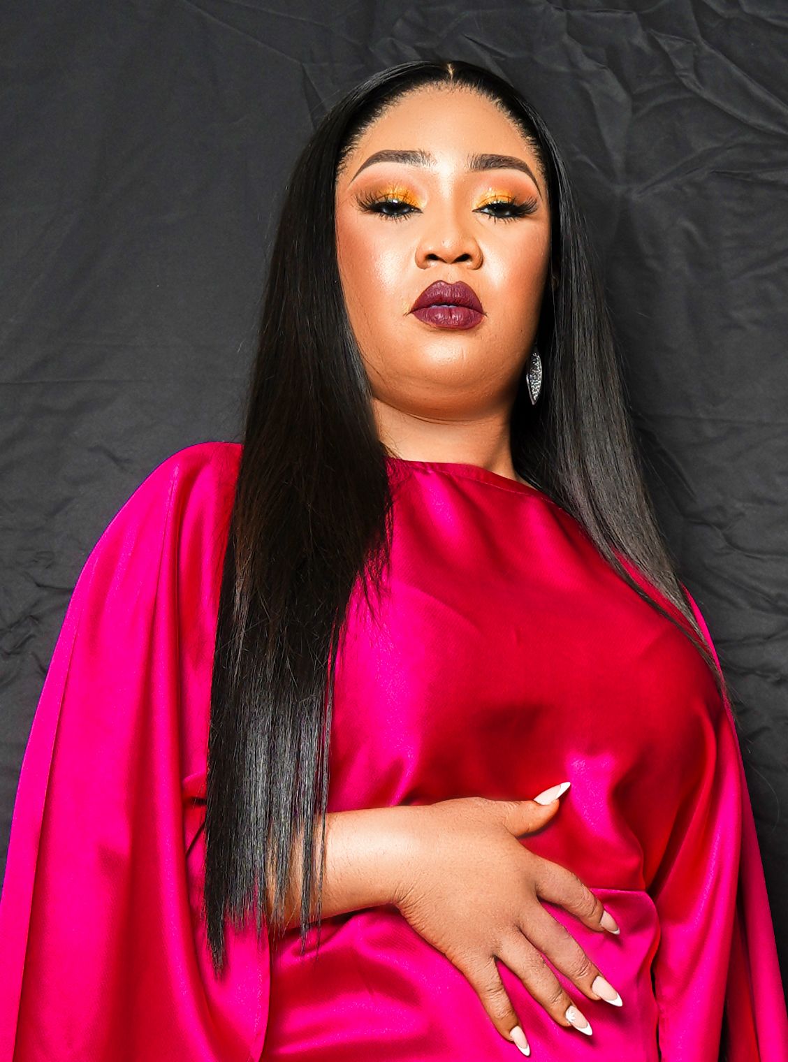 A model in a vibrant fuschia satin dress poses dramatically against a dark background.