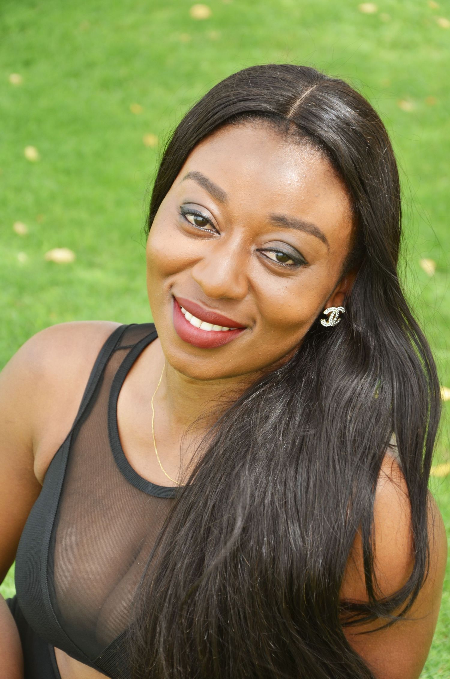 Person wearing black top poses on grass with styled hair and makeup.