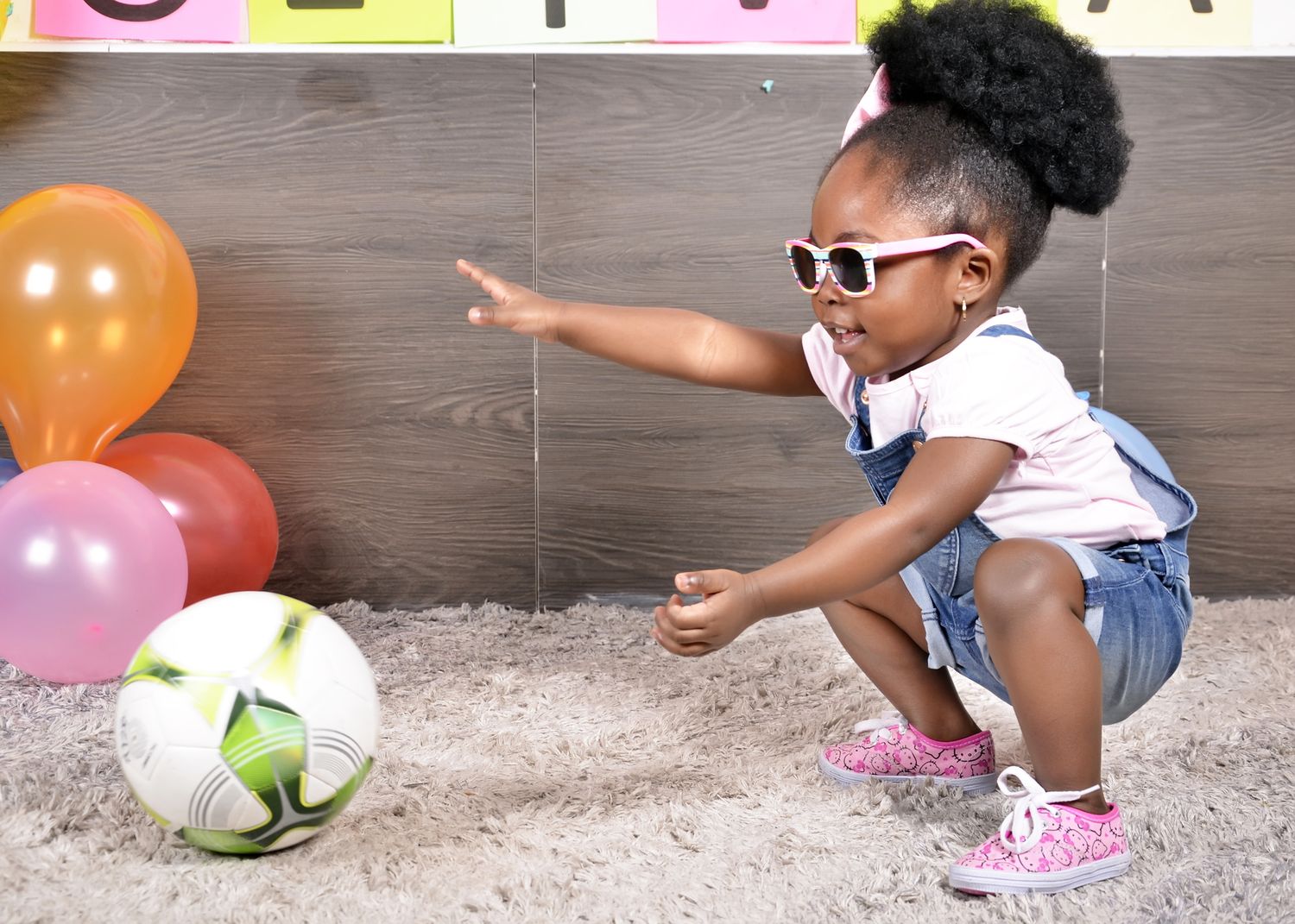 A playful moment with sunglasses and colorful balloons against a grey backdrop.