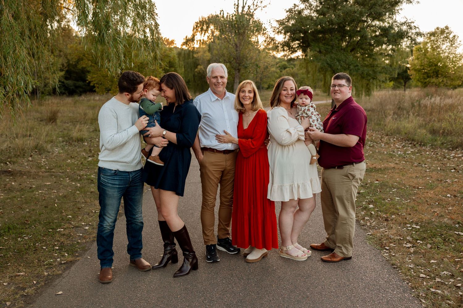 Family of seven posing outdoors at golden hour on a path surrounded by autumn trees.