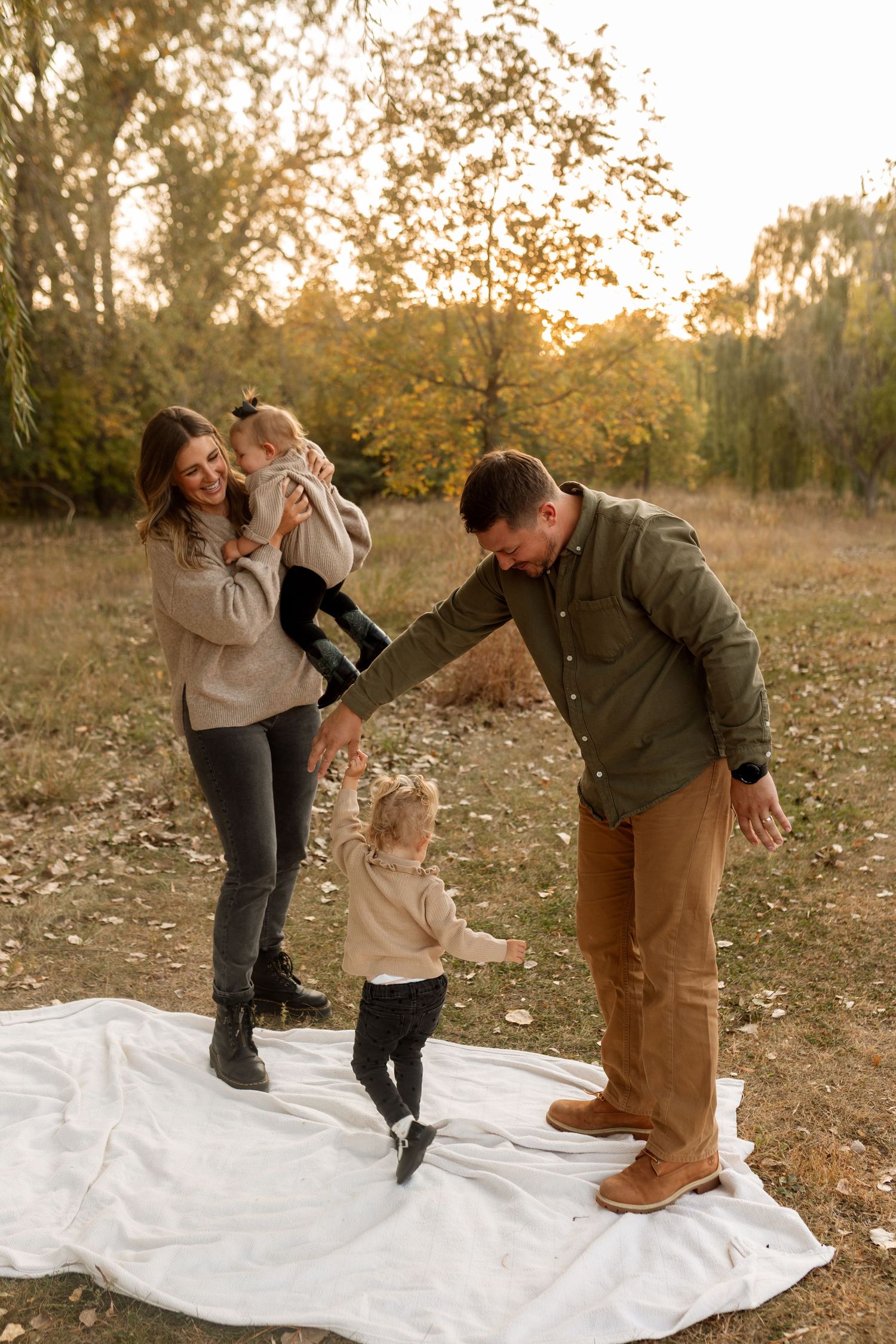 Family of four enjoying a warm autumn day outdoors on a white blanket surrounded by golden fall foliage.