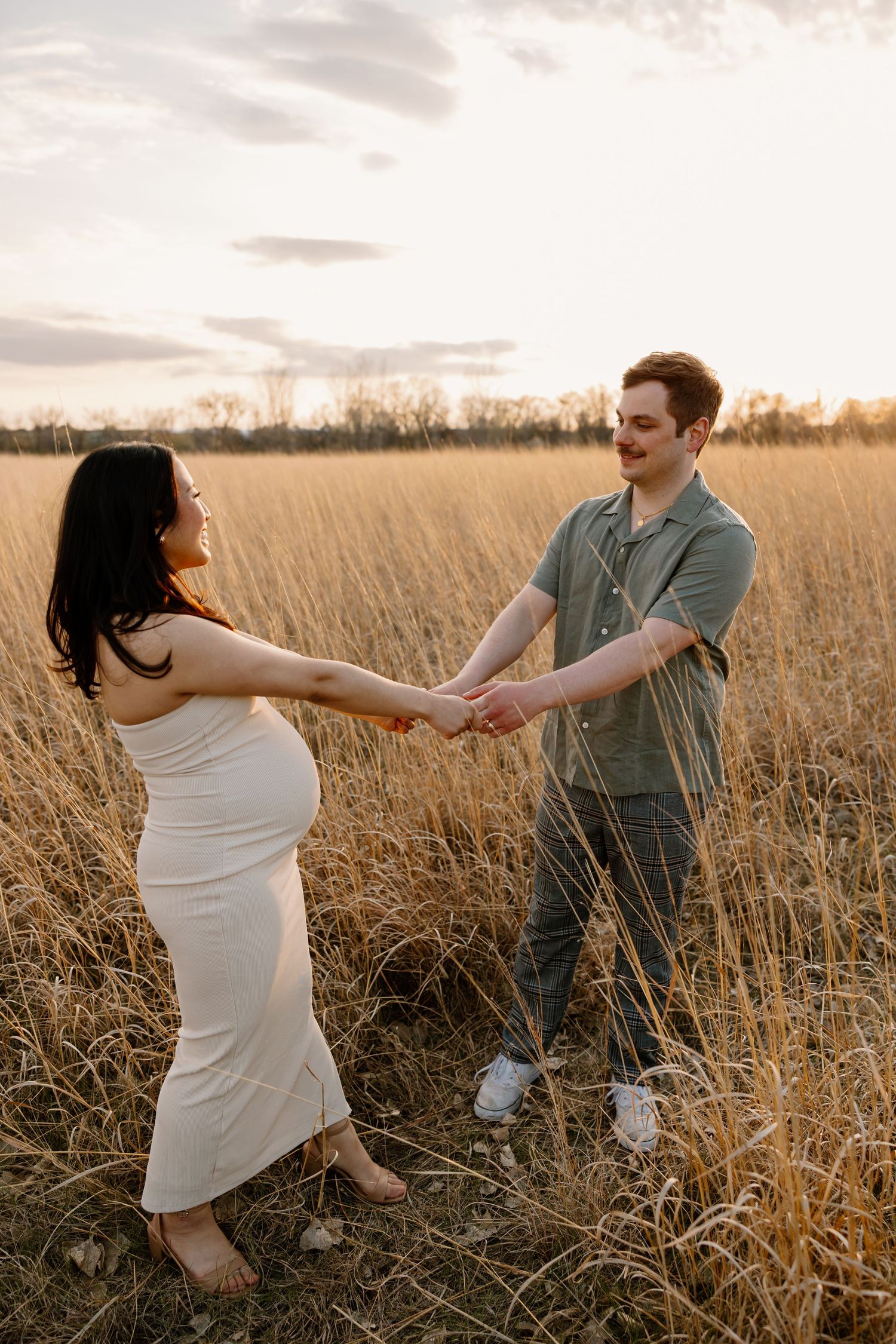 A couple dances playfully in a golden field during sunset.