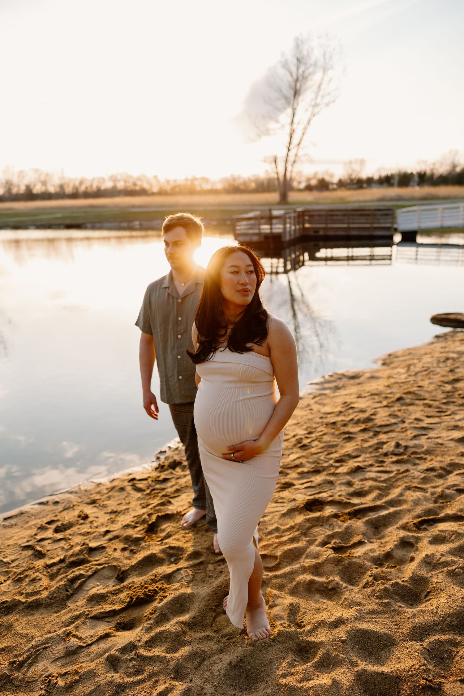 A couple walks along a sandy beach shore during a glowing sunset.