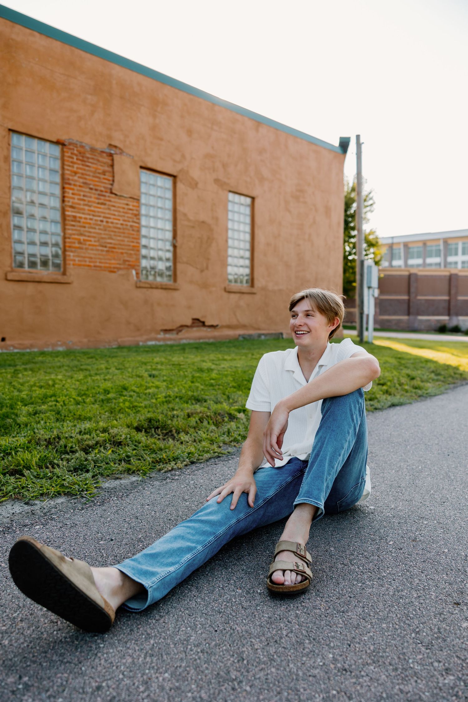 Casual outdoor portraits of someone sitting on pavement against brick building wall.