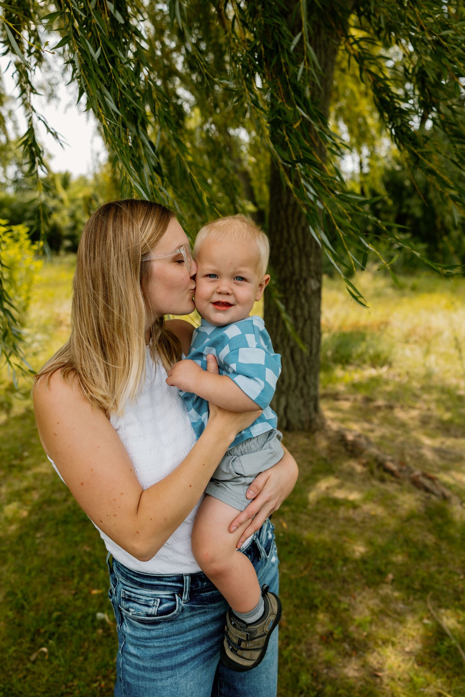 A tender moment between parent and child under a weeping willow tree on a sunny summer day.