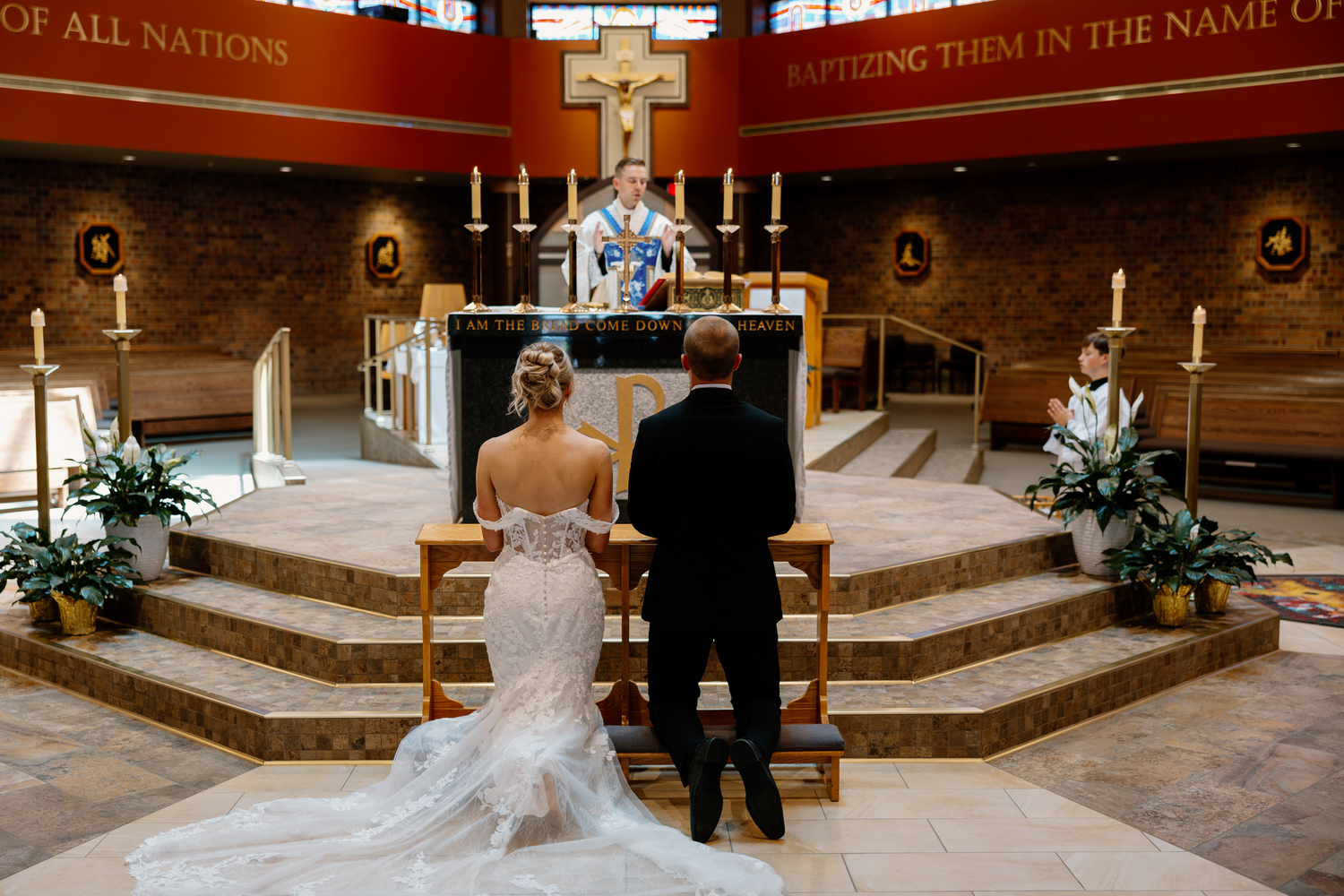 Bride and groom stand at altar before priest during Catholic wedding ceremony in modern church.