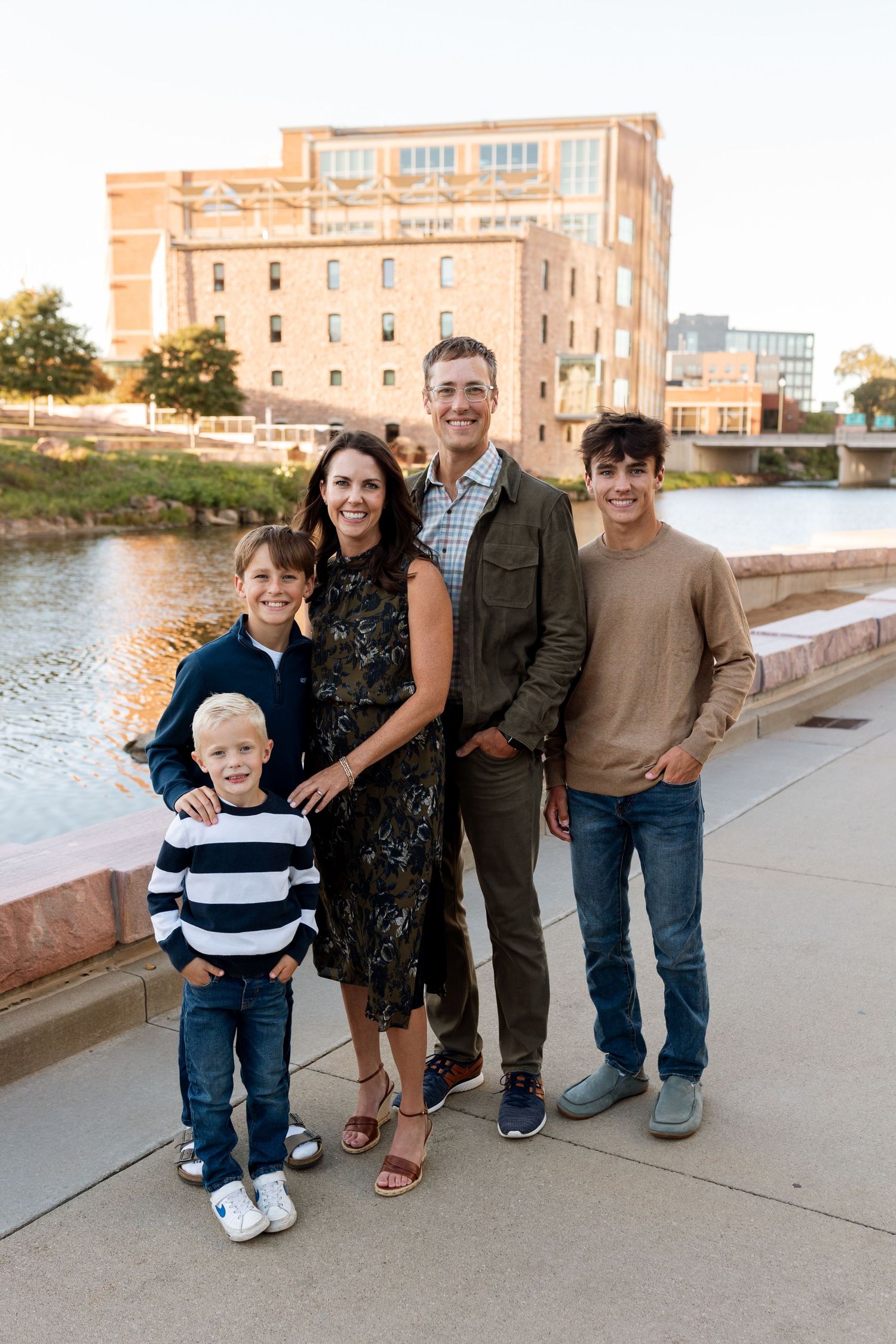 Group standing together on riverside path with brick building in background.