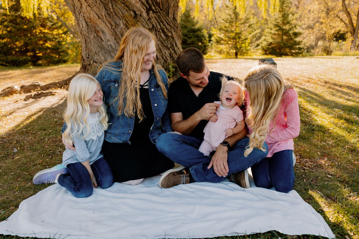 Family sitting together on a white blanket in a sunlit park during a golden autumn afternoon.