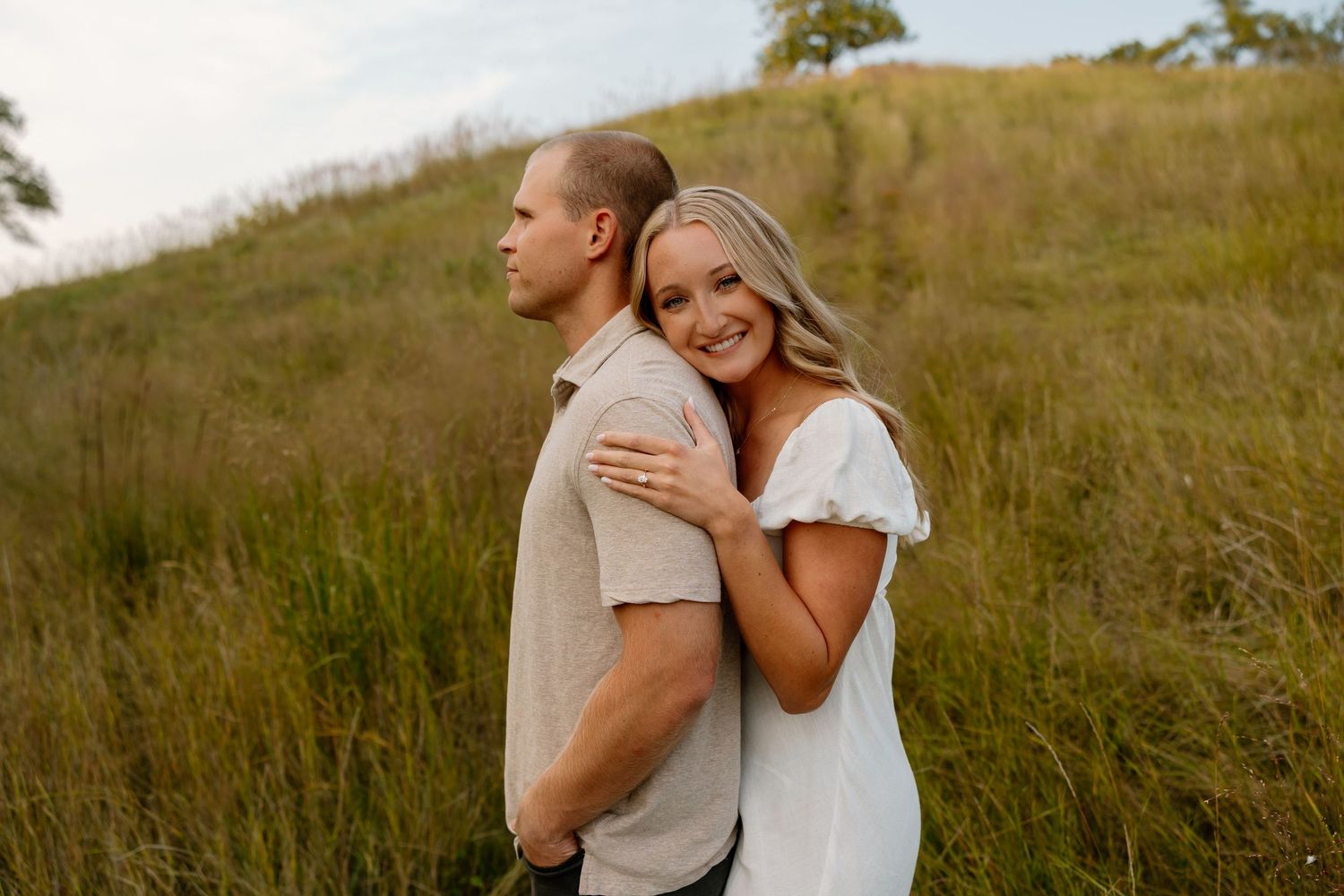 A couple embraces on a grassy hillside during a romantic photoshoot at golden hour.