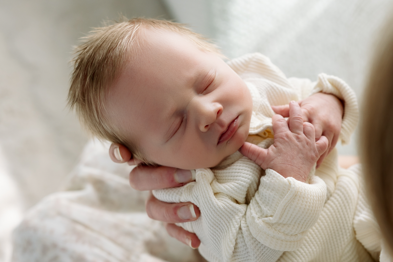 A sleeping baby wearing a cream-colored knit sweater rests peacefully on white bedding.