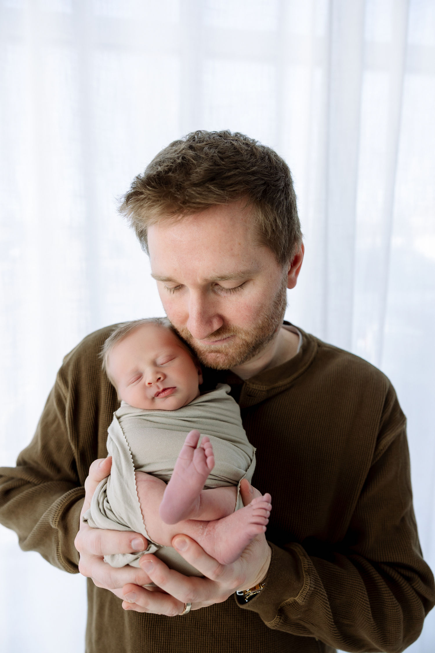 A tender moment captured in a triptych showing a parent in brown clothing holding and kissing a sleeping newborn baby.