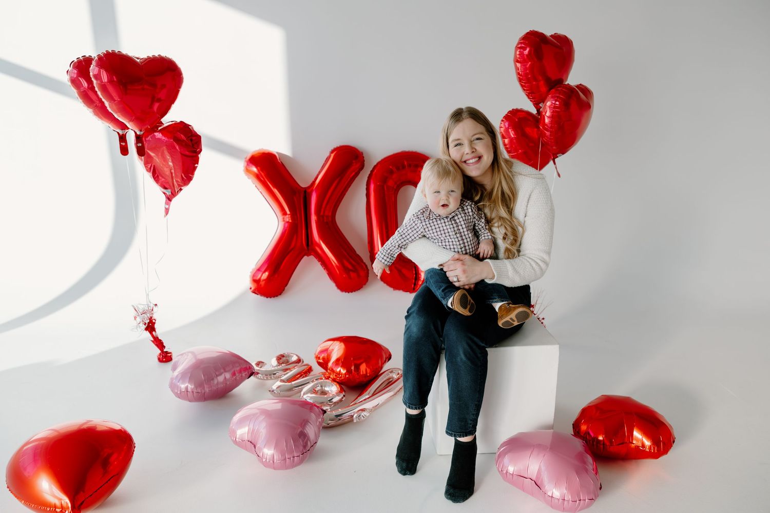 Valentine's day decorations with red heart balloons, XO letters, and pink pillows in a bright studio setting.