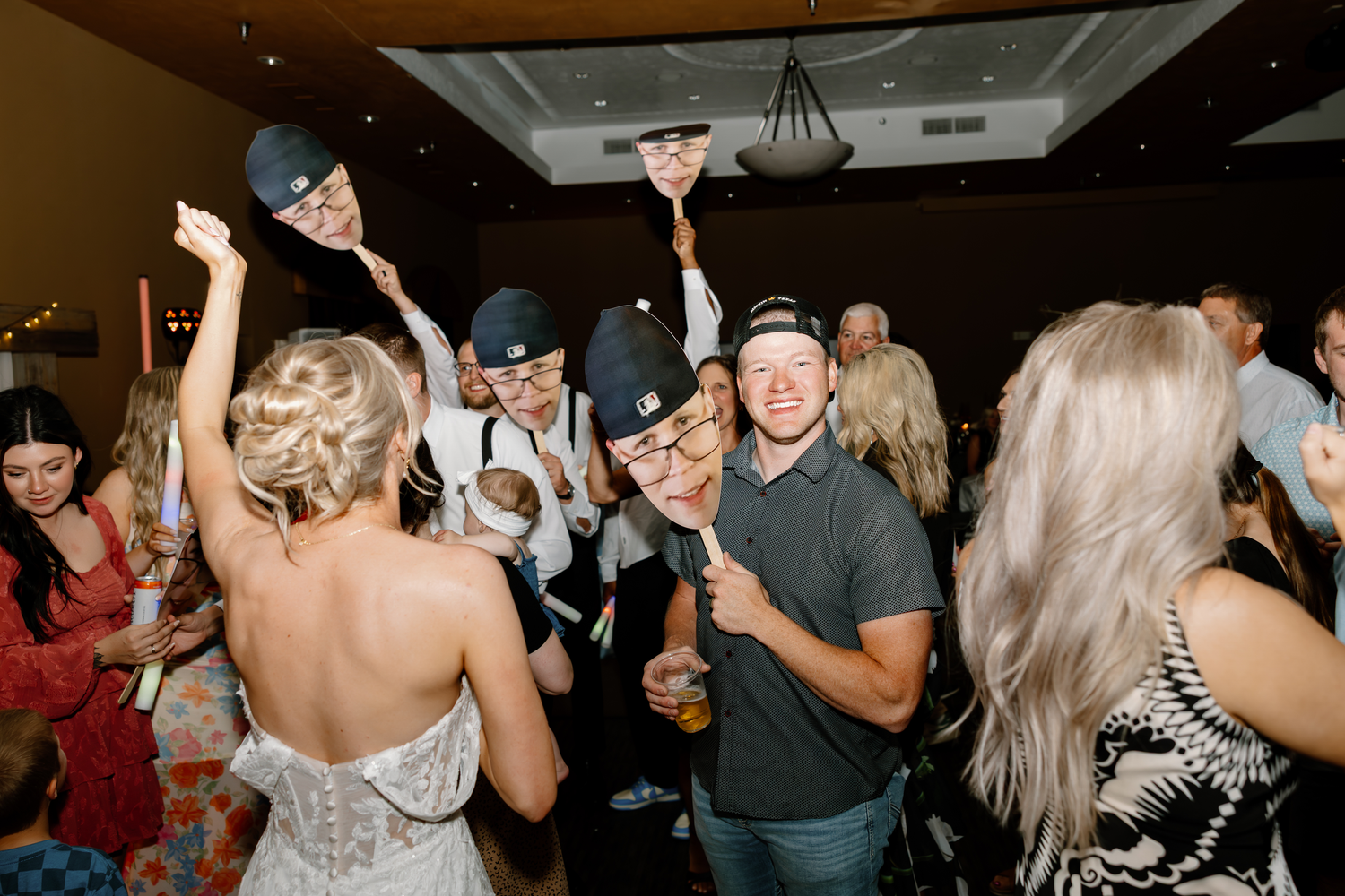 Guests dancing and celebrating at a lively wedding reception party indoors wearing caps and having fun.