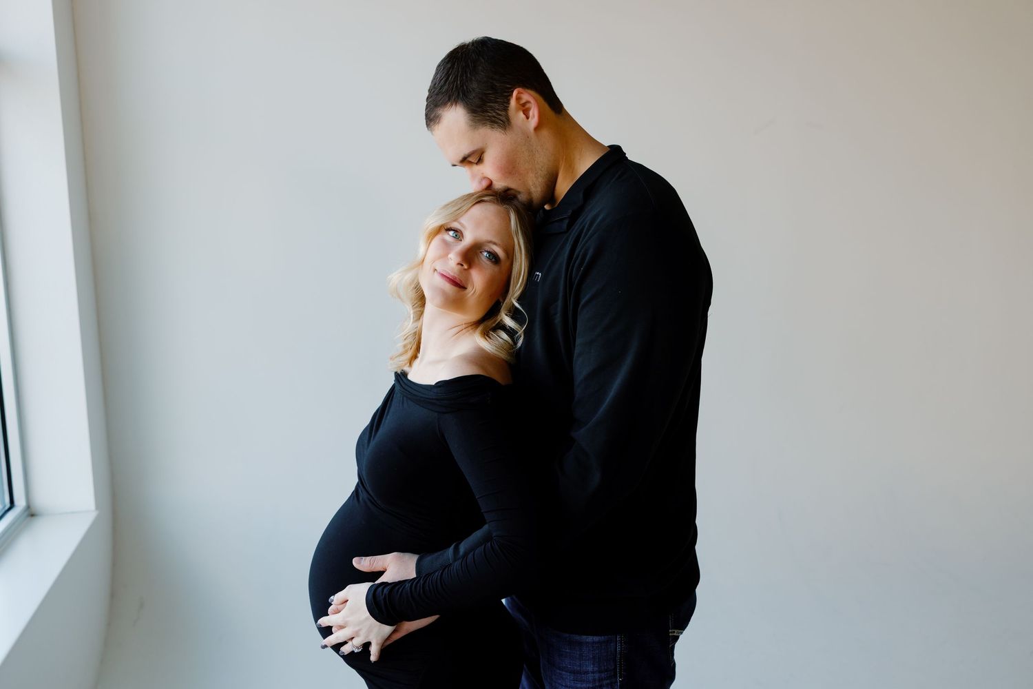 A couple embraces tenderly by a bright window in a romantic indoor photoshoot. Riley Ro Photo Sioux Falls, SD