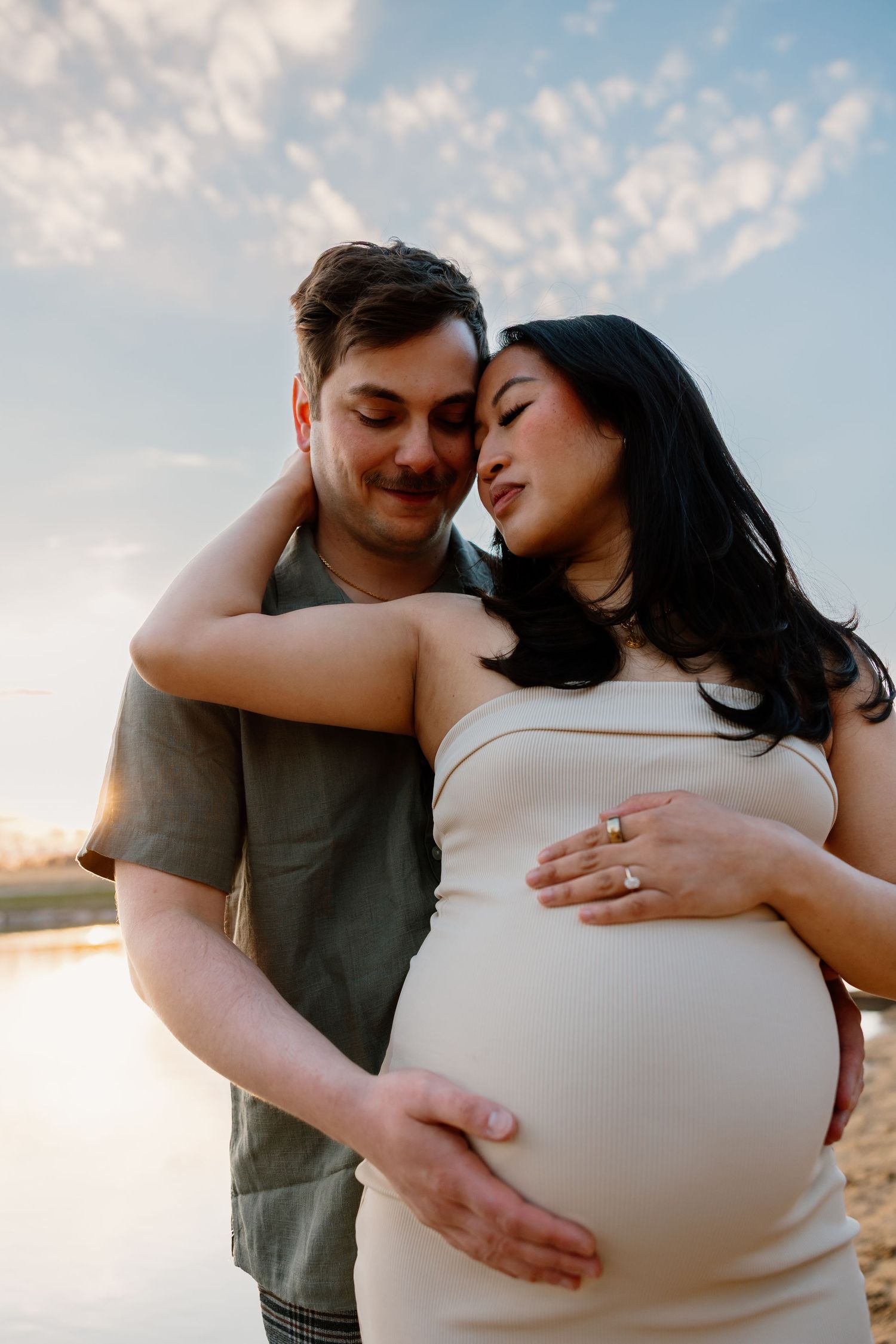 Expecting couple embraces during sunset maternity photoshoot as they tenderly hold her pregnant belly.