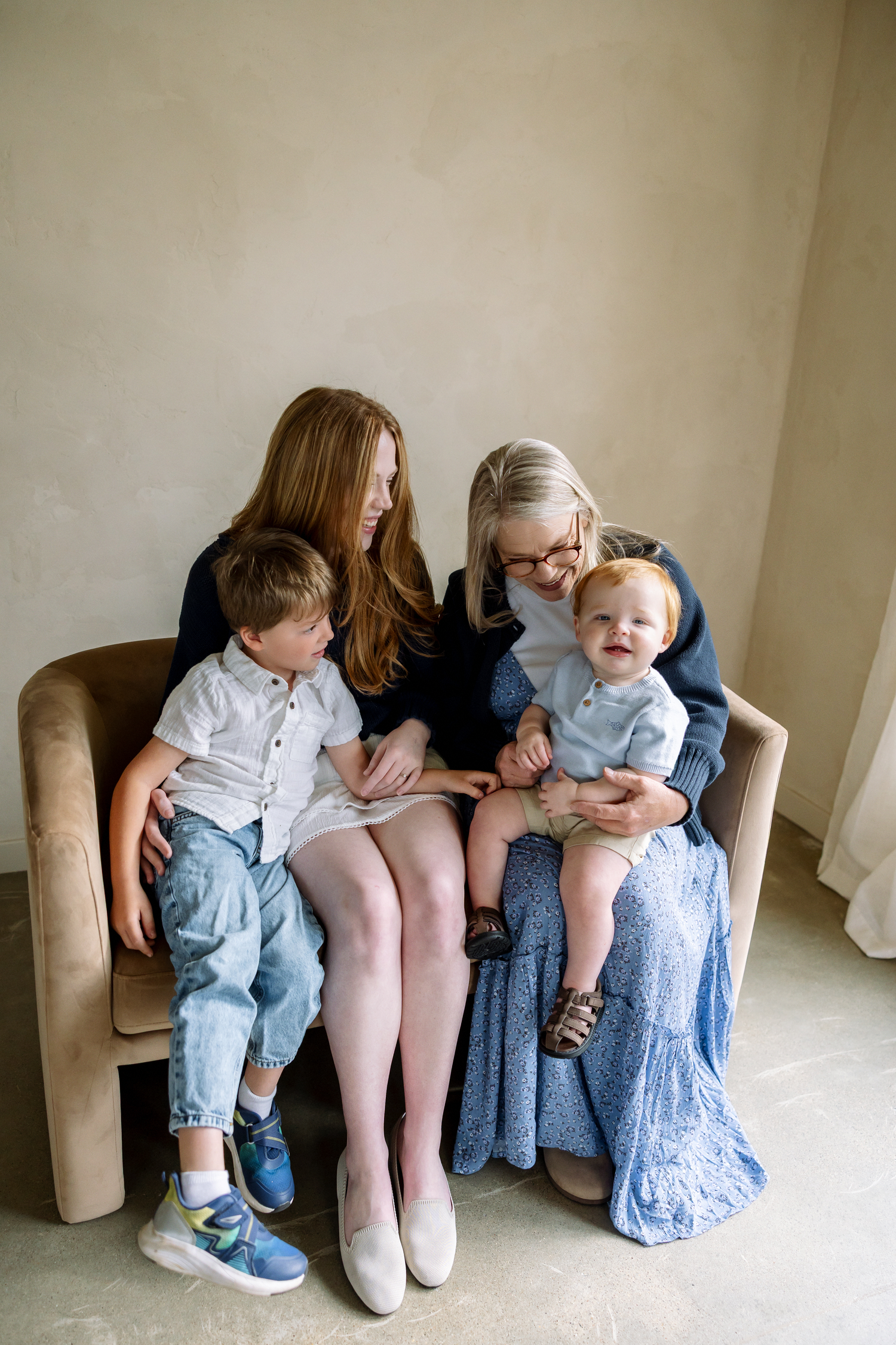 Two women sitting in a chair with two young red-haired children, sharing a warm family moment indoors.