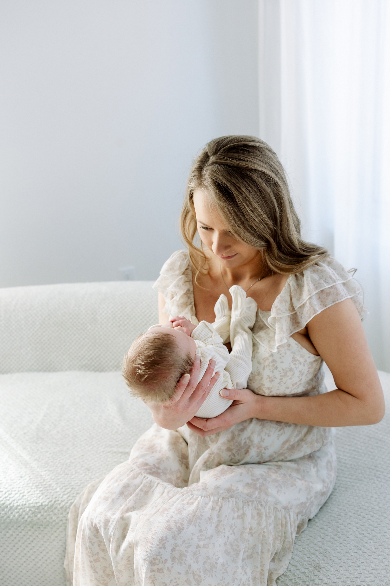 Mother in white dress lying on bed with baby in tender embrace showing loving maternal bond.
