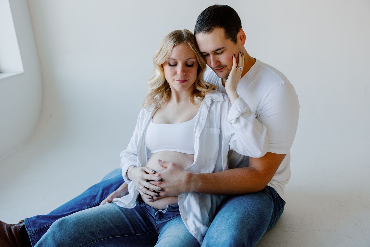 A couple sits together on a couch in a bright room while sharing tender moments with their baby. Riley Ro Photo Sioux Falls, SD