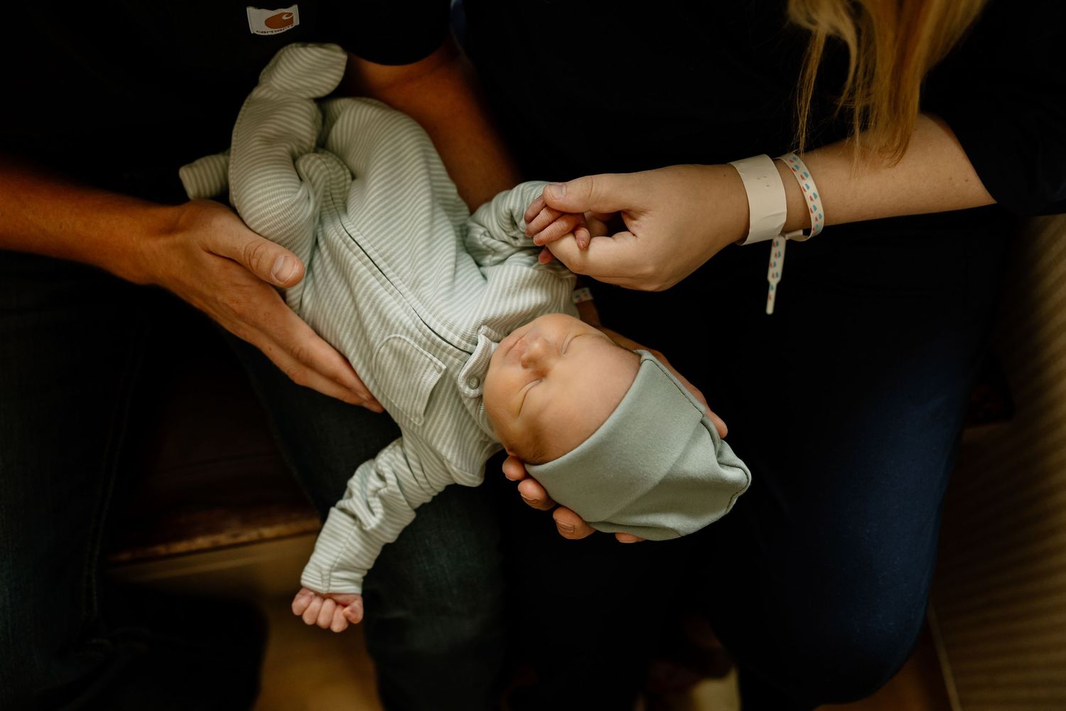 Nurturing hands hold and comfort a tiny newborn baby wrapped in white.