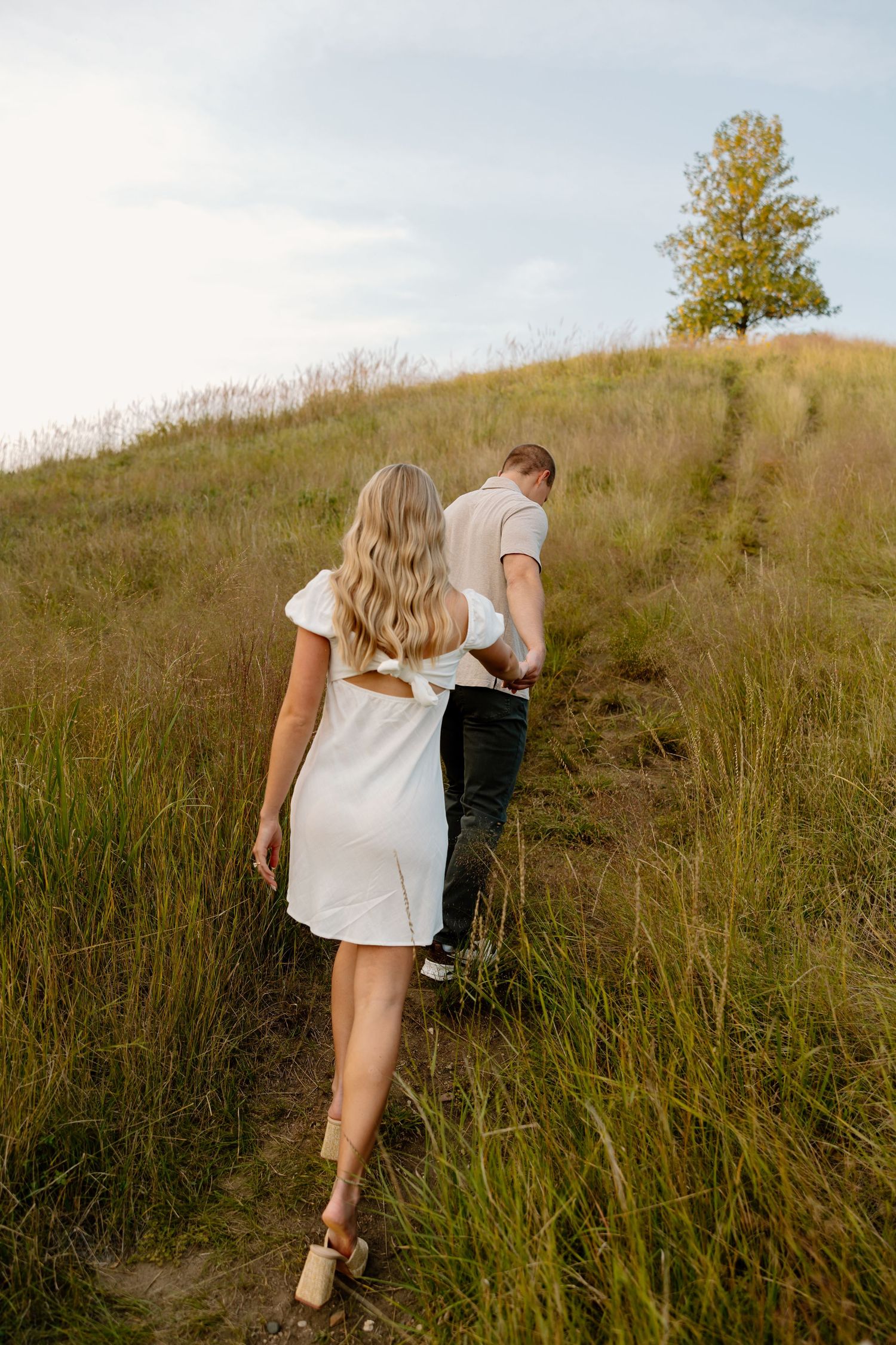 Couple walking up a grassy hillside path on a sunny summer afternoon.