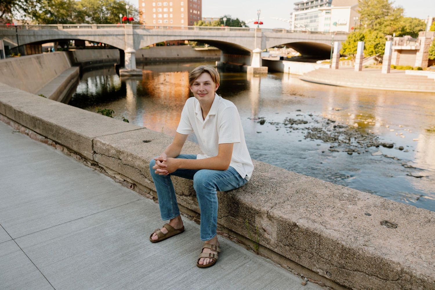 Person sitting on concrete steps near urban waterfront during sunset with buildings in background.