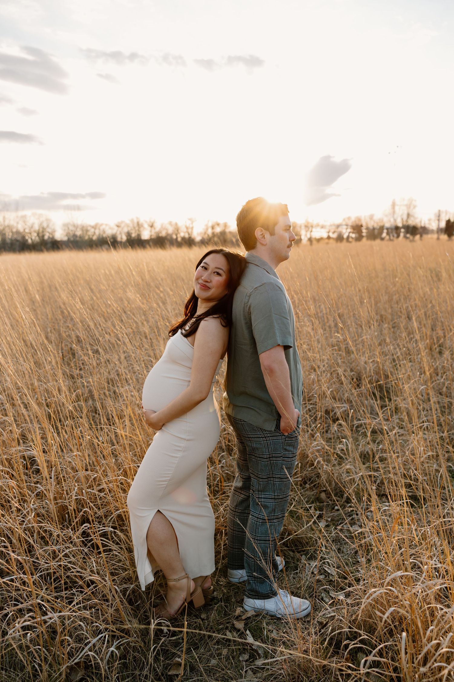 Couple poses in golden wheat field during sunset maternity photo session.