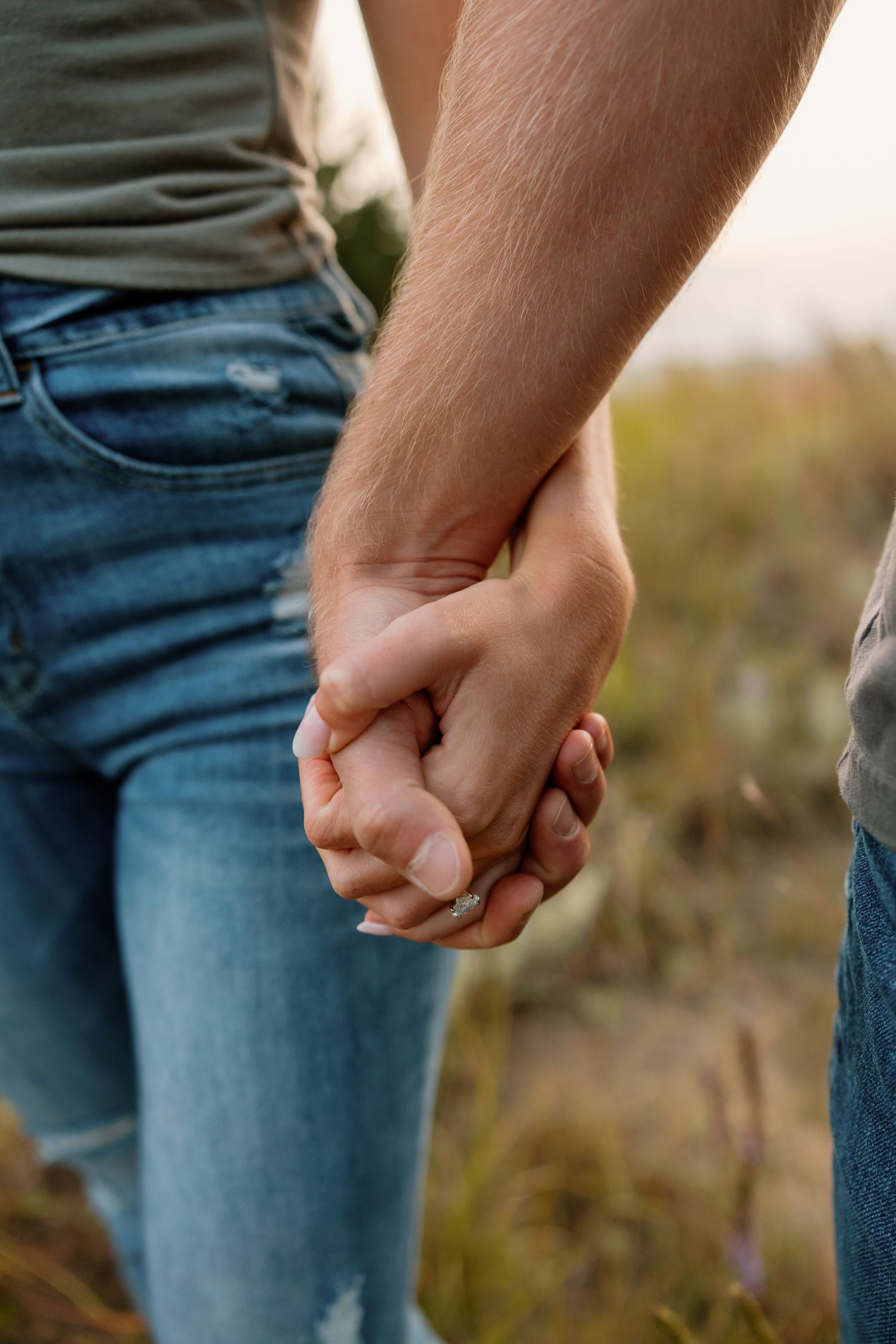Close-up view of two people holding hands against blue denim in an outdoor setting. sioux falls photographer riley ro photo