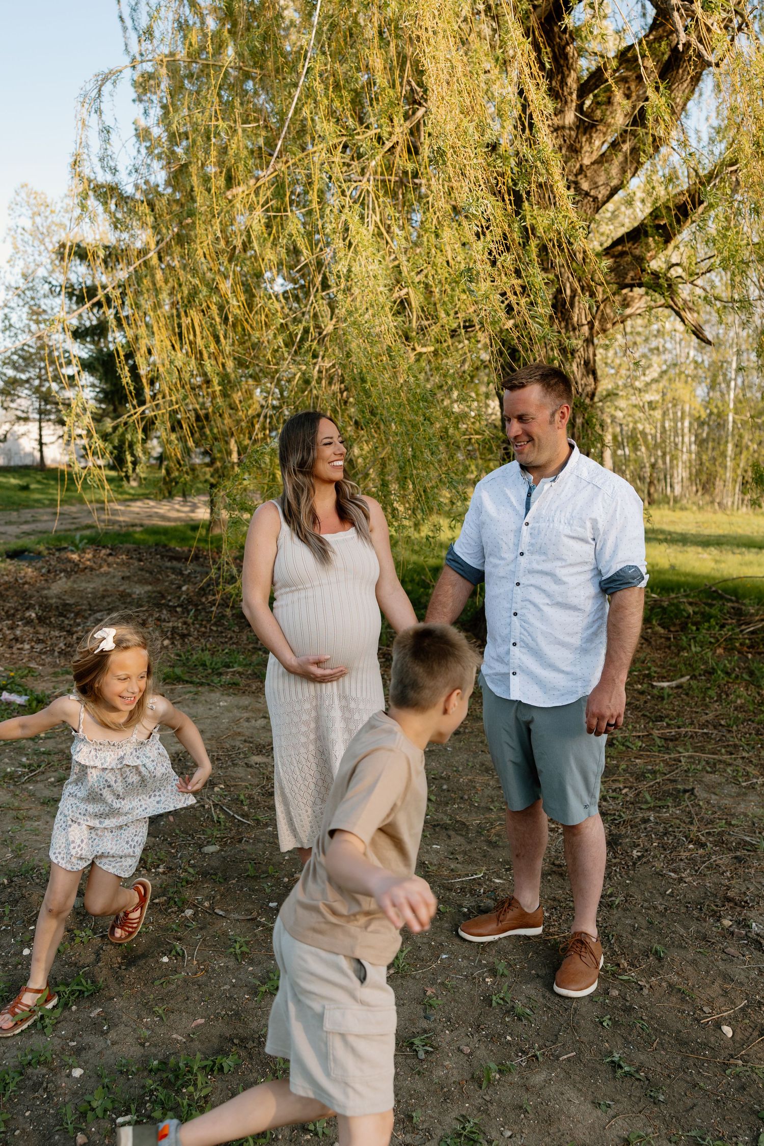 A family of four enjoys a playful moment under a weeping willow tree on a sunny afternoon.