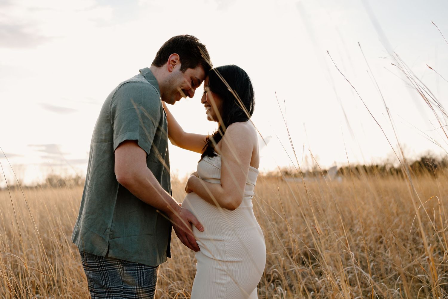 A couple shares an intimate moment in a golden wheat field at sunset, with light filtering through the tall grass.
