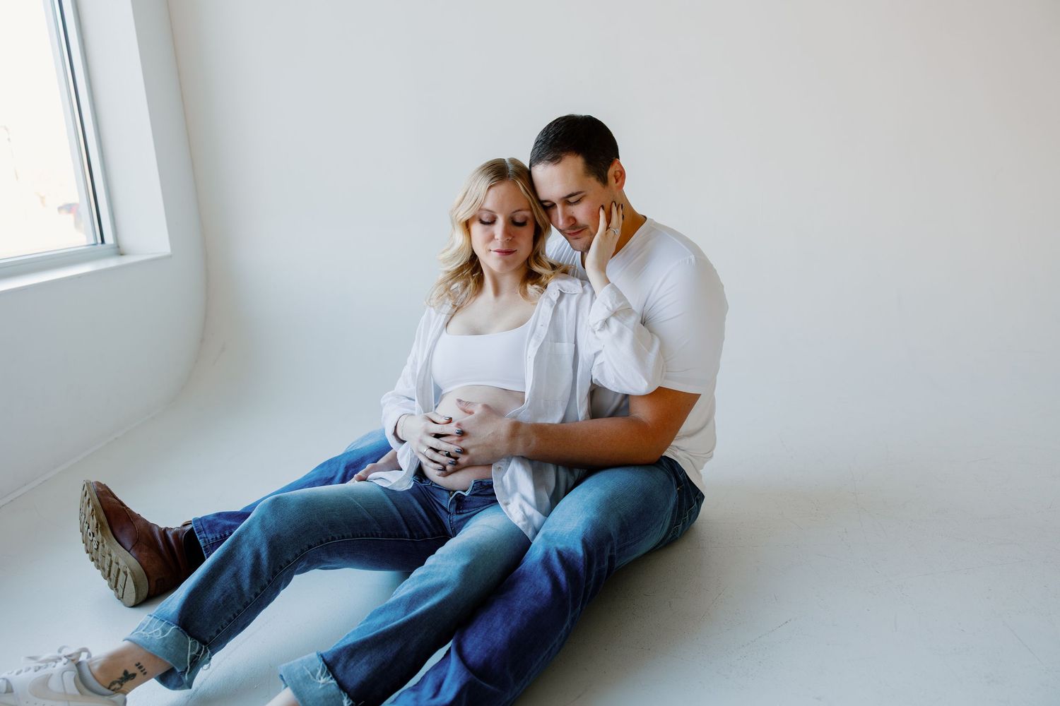 A couple sits together on a white couch reading a book in a bright, minimalist room. Riley Ro Photo Sioux Falls, SD