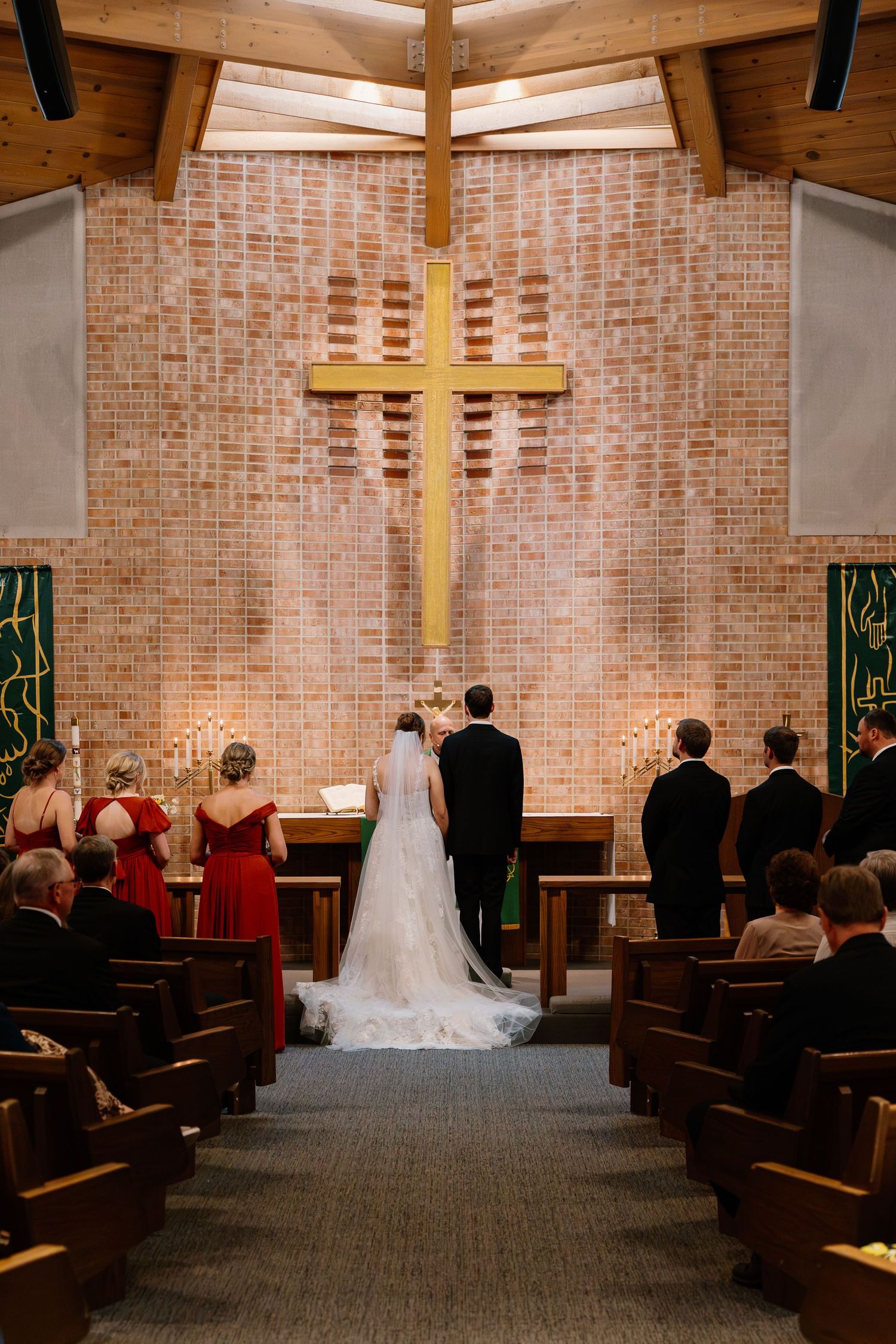 Wedding ceremony in a modern church with exposed brick walls, wooden pews, and illuminated crosses at the altar.