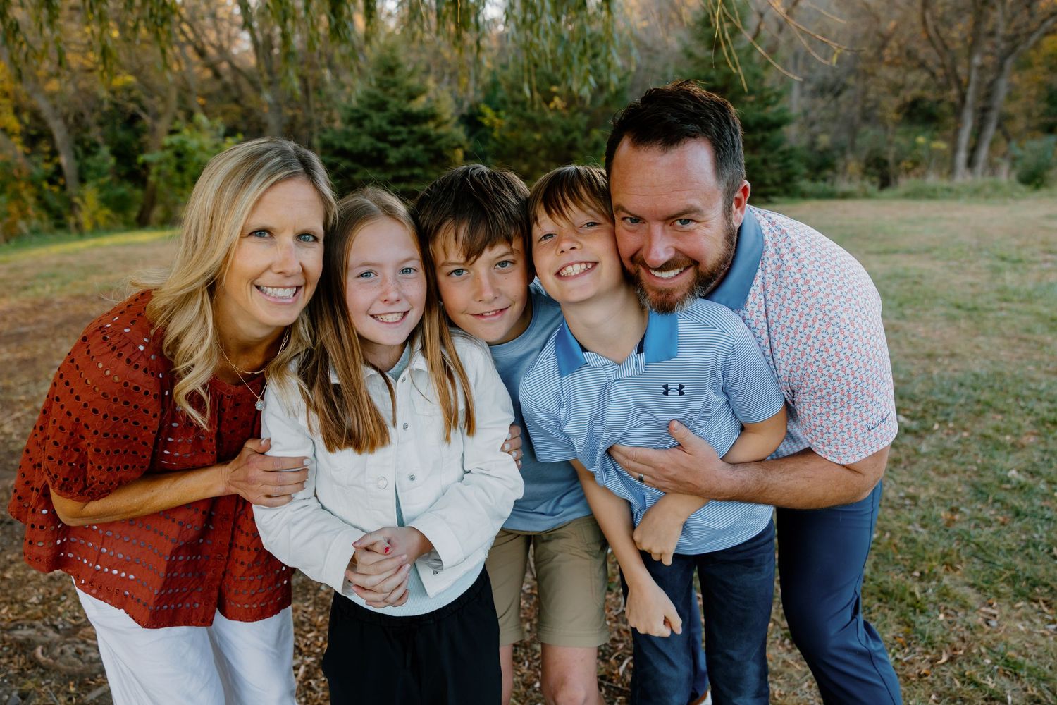 Happy family of five smiling outdoors in a park during fall, parents with three children posing together.