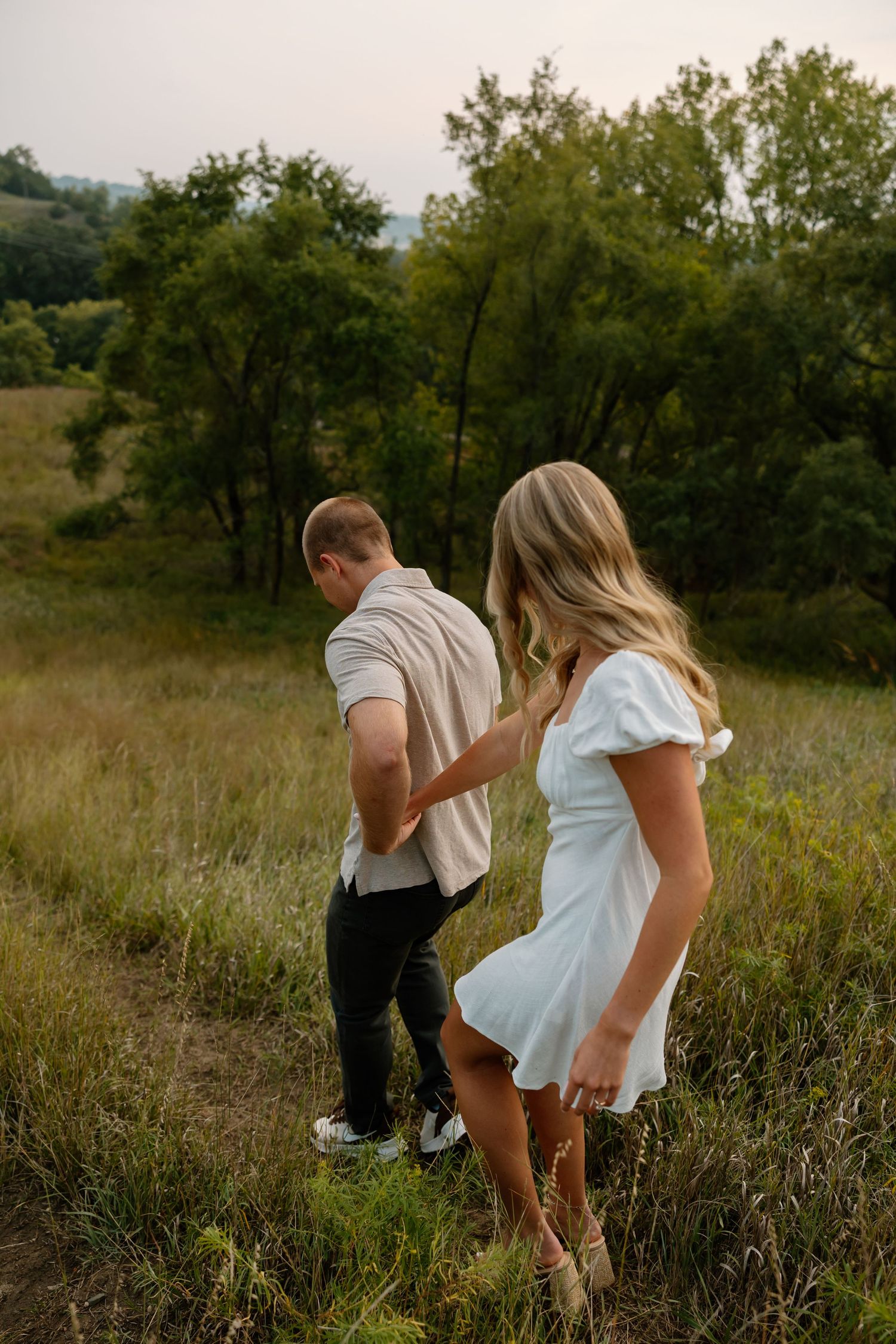 Playful couple walking through tall grass in a meadow during golden hour.