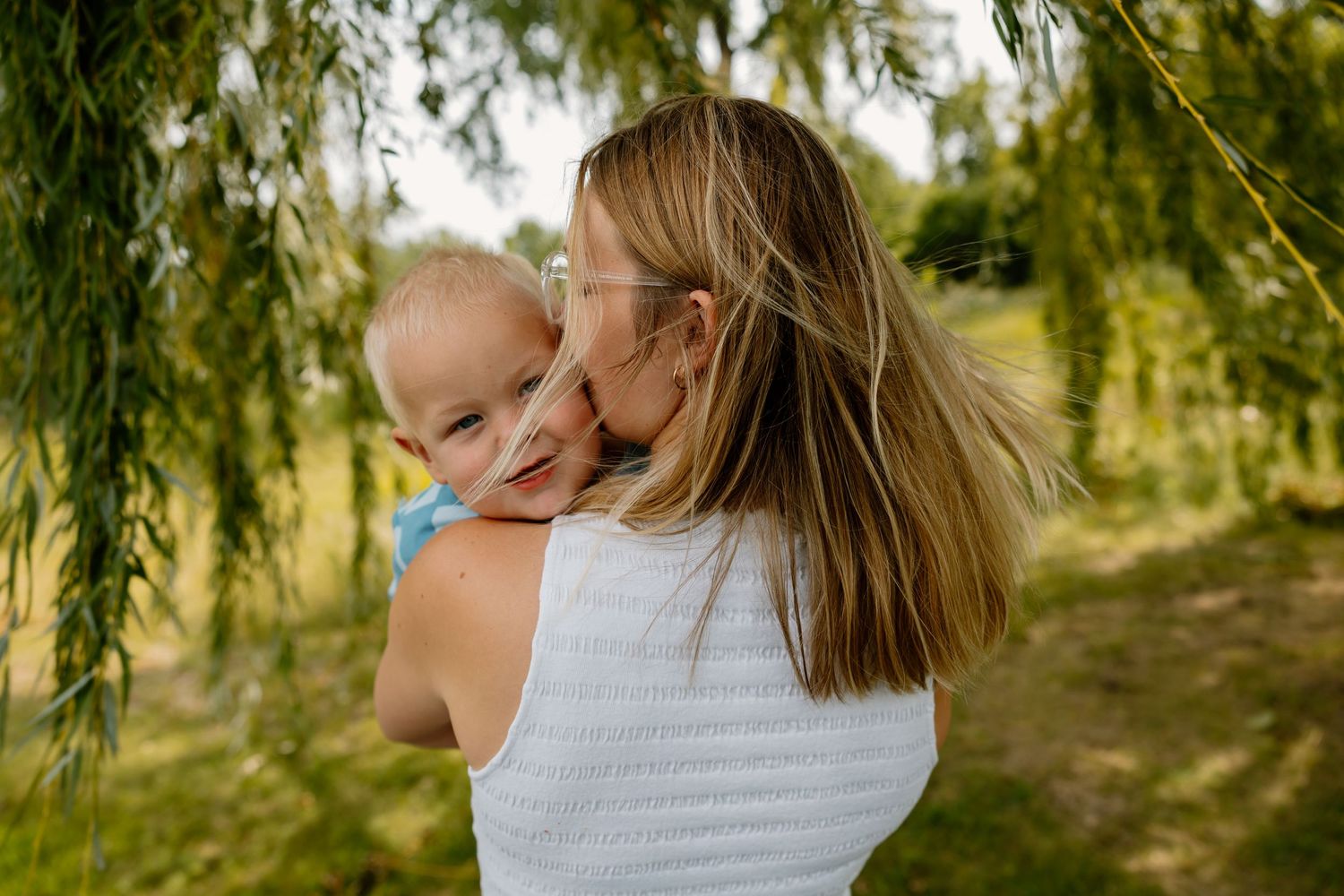 A tender moment shared under willow branches on a sunny day outdoors.